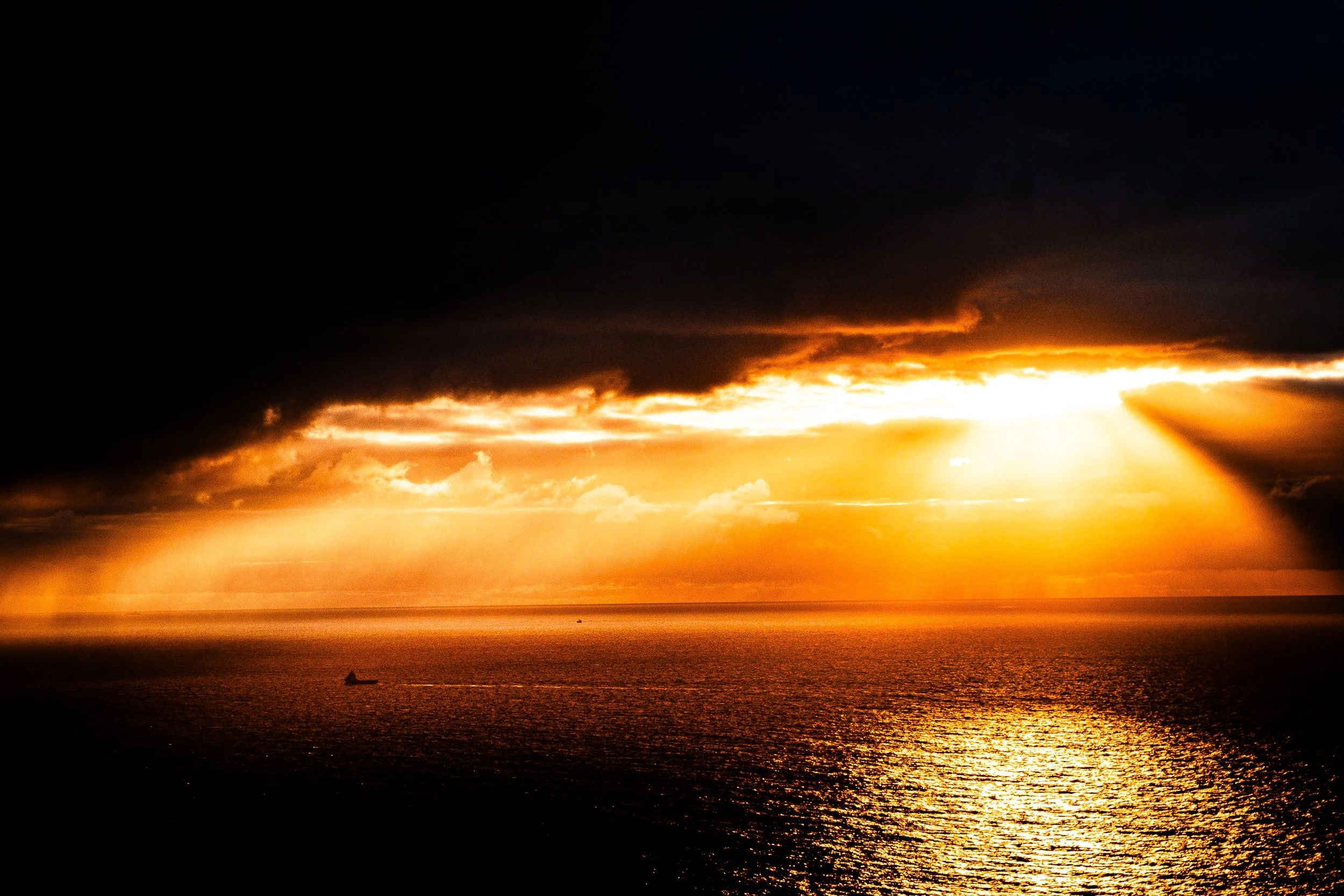 Dramatic orange sunset over the ocean beneath dark storm clouds