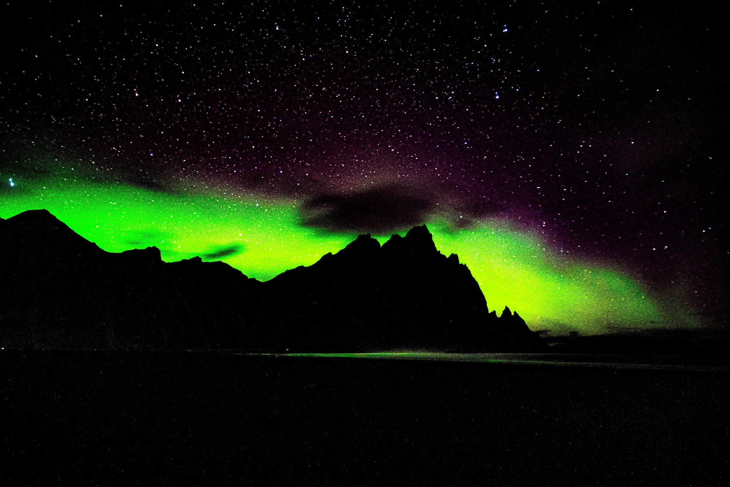 Bright green aurora borealis over a silhouetted mountain range beneath a star-filled night sky
