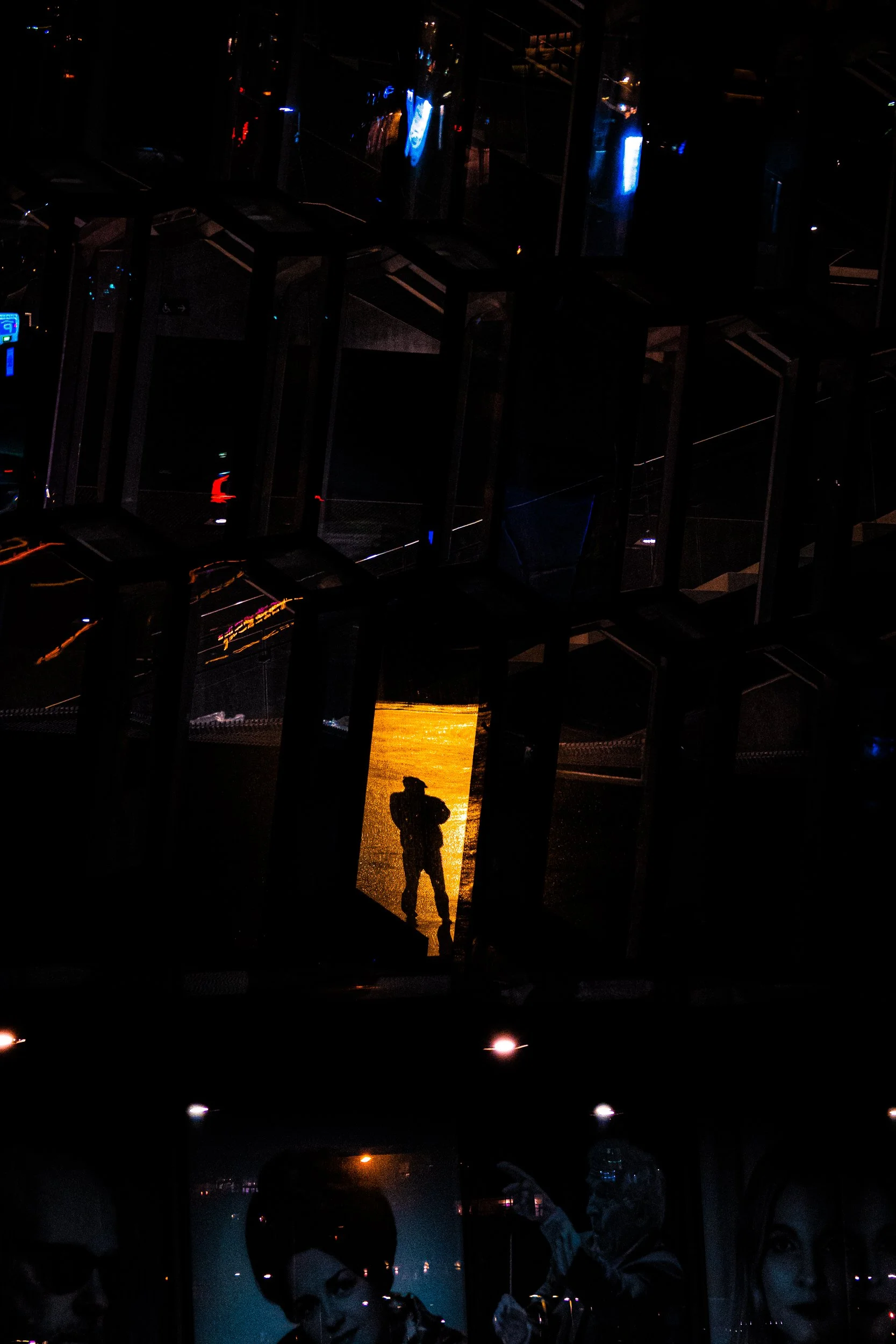 Dark nighttime scene with silhouetted people and illuminated reflections behind a glass or metal structure.