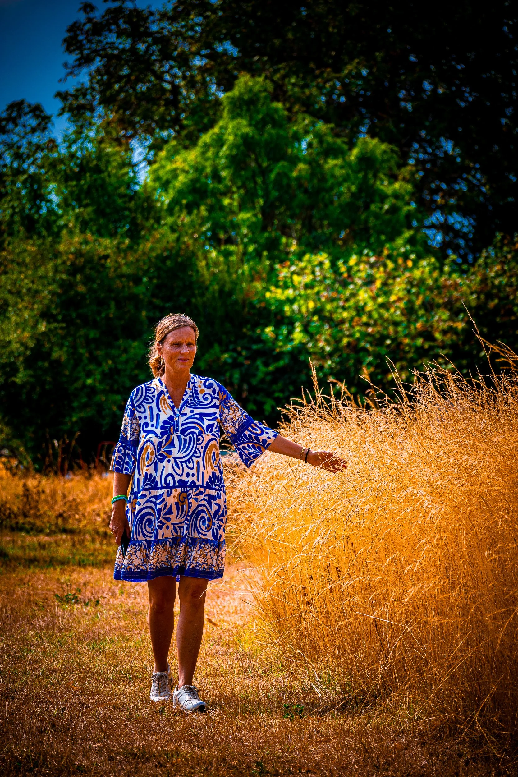 Woman in a blue-and-white patterned dress standing in a sunlit field of tall golden grass