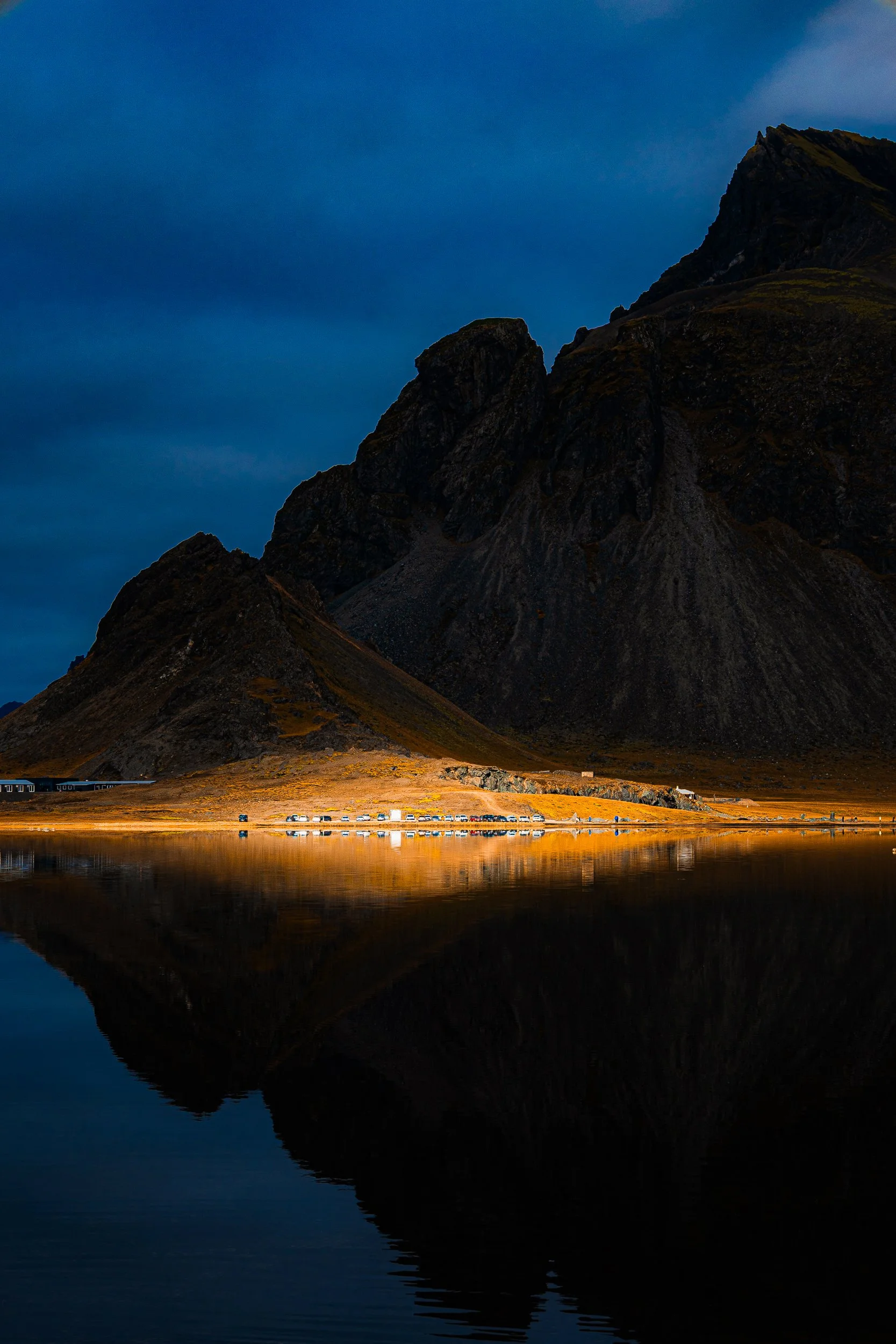 Jagged dark mountain and lakeshore reflected in a calm alpine lake at golden hour