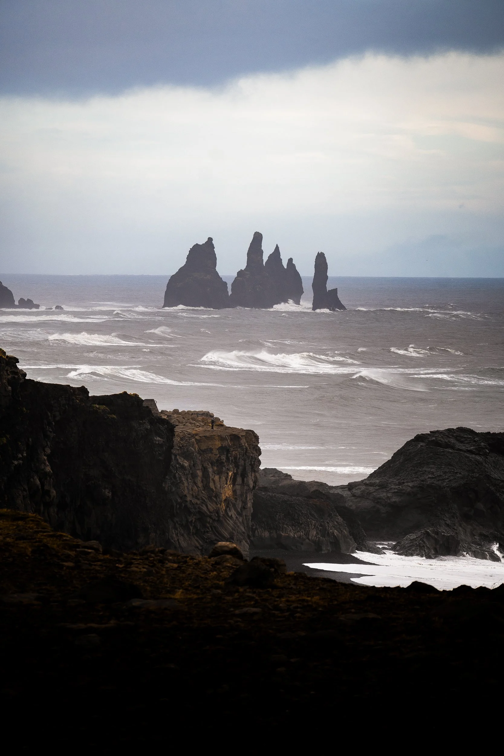 Dramatic basalt sea stacks rising from the ocean along Iceland’s rugged black volcanic coastline under an overcast sky