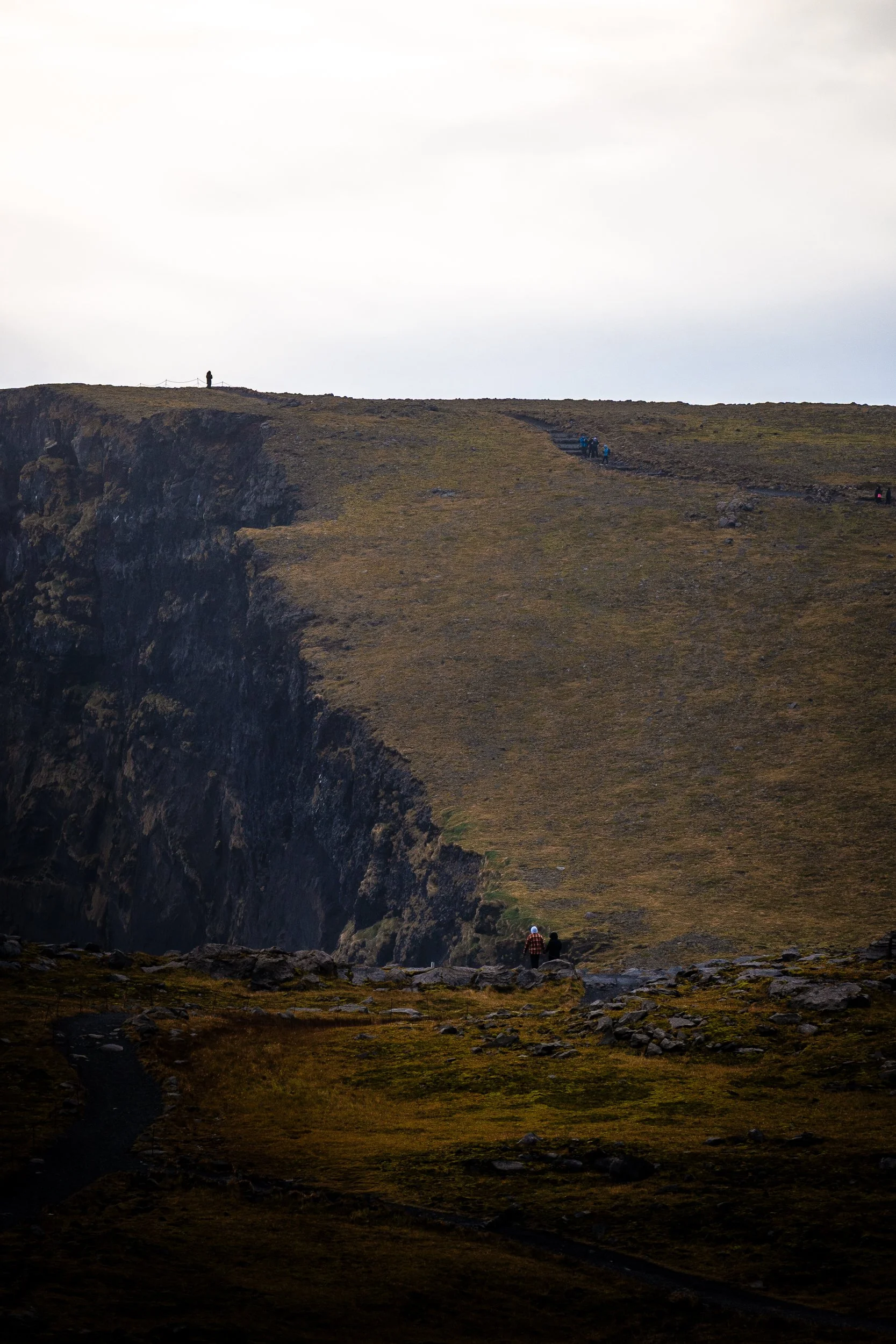 Hikers walking along a grassy cliff edge above a rugged mountain gorge in Iceland