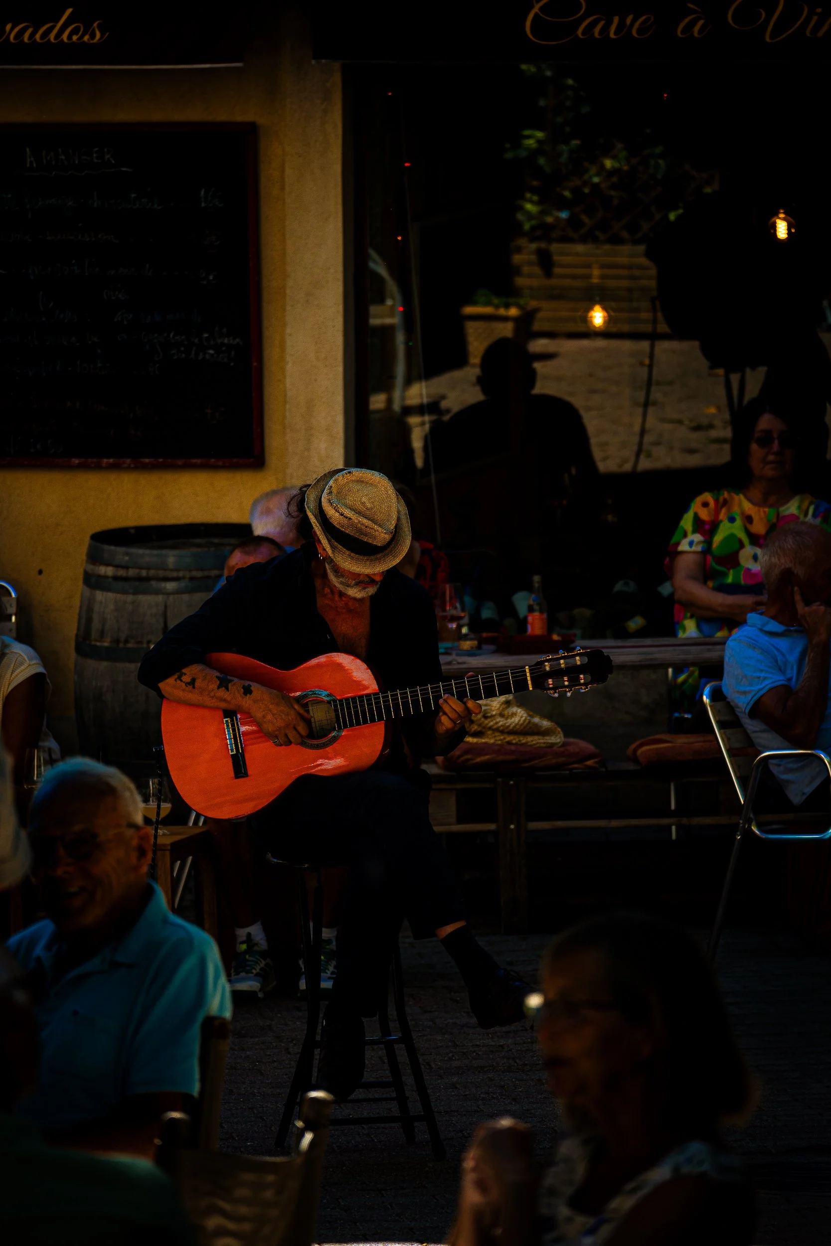 Street musician in a straw hat playing an acoustic guitar outside a café as people dine nearby