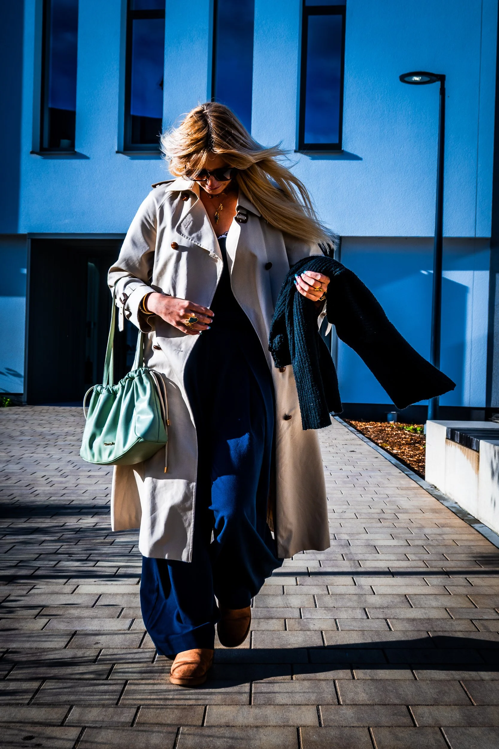 Woman in sunglasses wearing a beige trench coat and carrying a mint green handbag outdoors