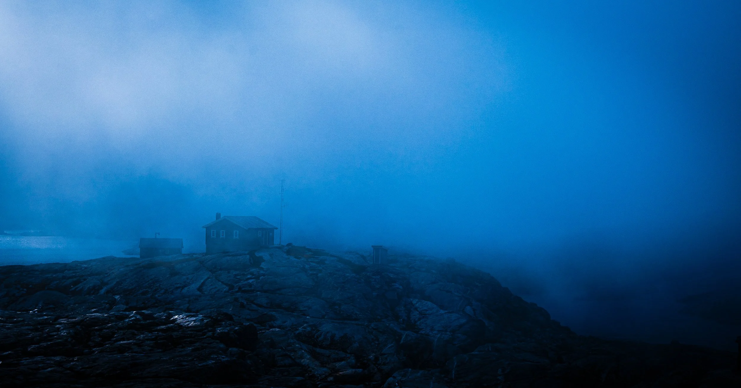 Remote cabin on a rocky coastline shrouded in blue fog