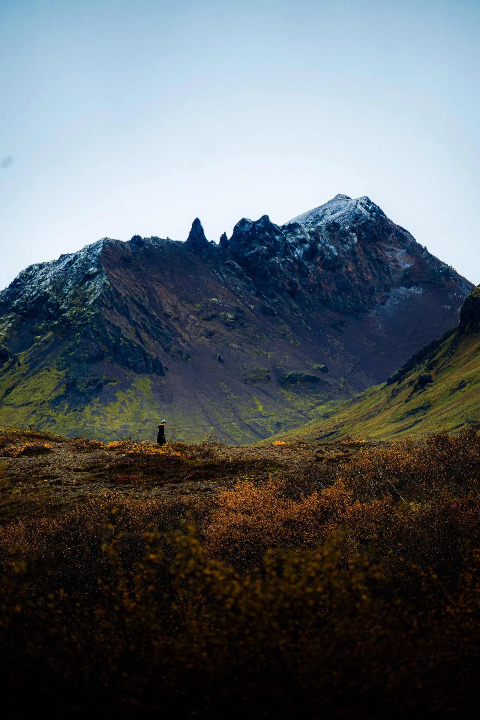 Dramatic rugged mountain range above an autumn tundra valley, with a lone hiker in the foreground.