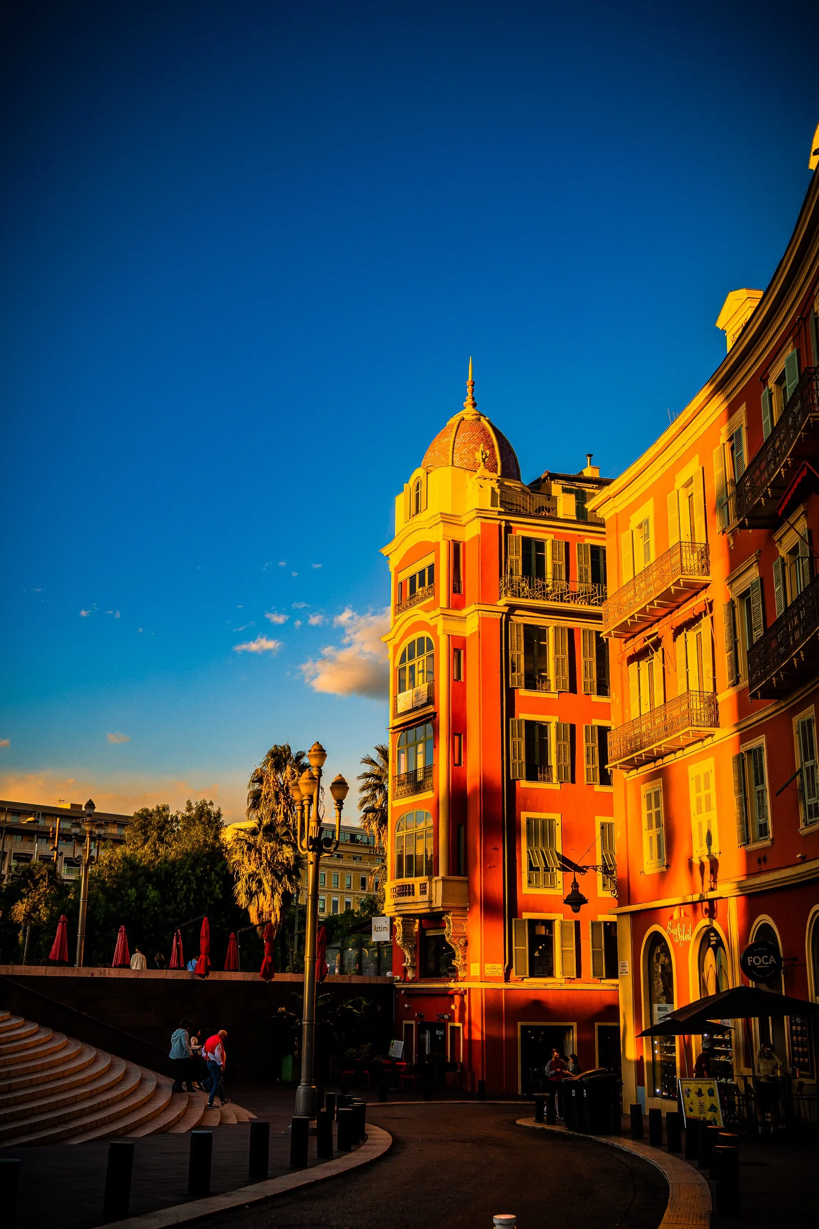 Colorful historic buildings with ornate balconies and a domed turret lining a sunny plaza beneath a deep blue sky