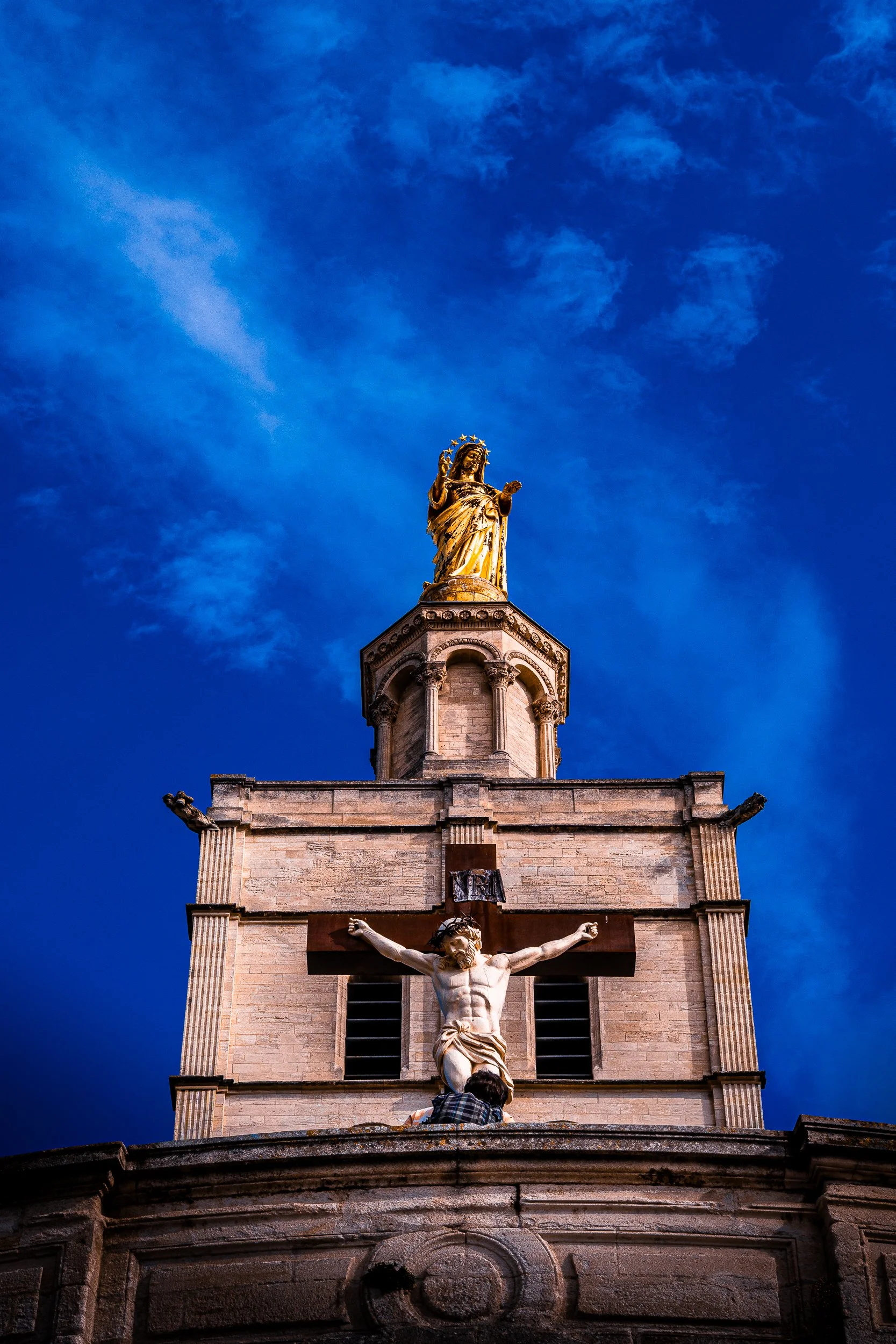 Church facade with a crucifix and Virgin Mary statue against a vivid blue sky
