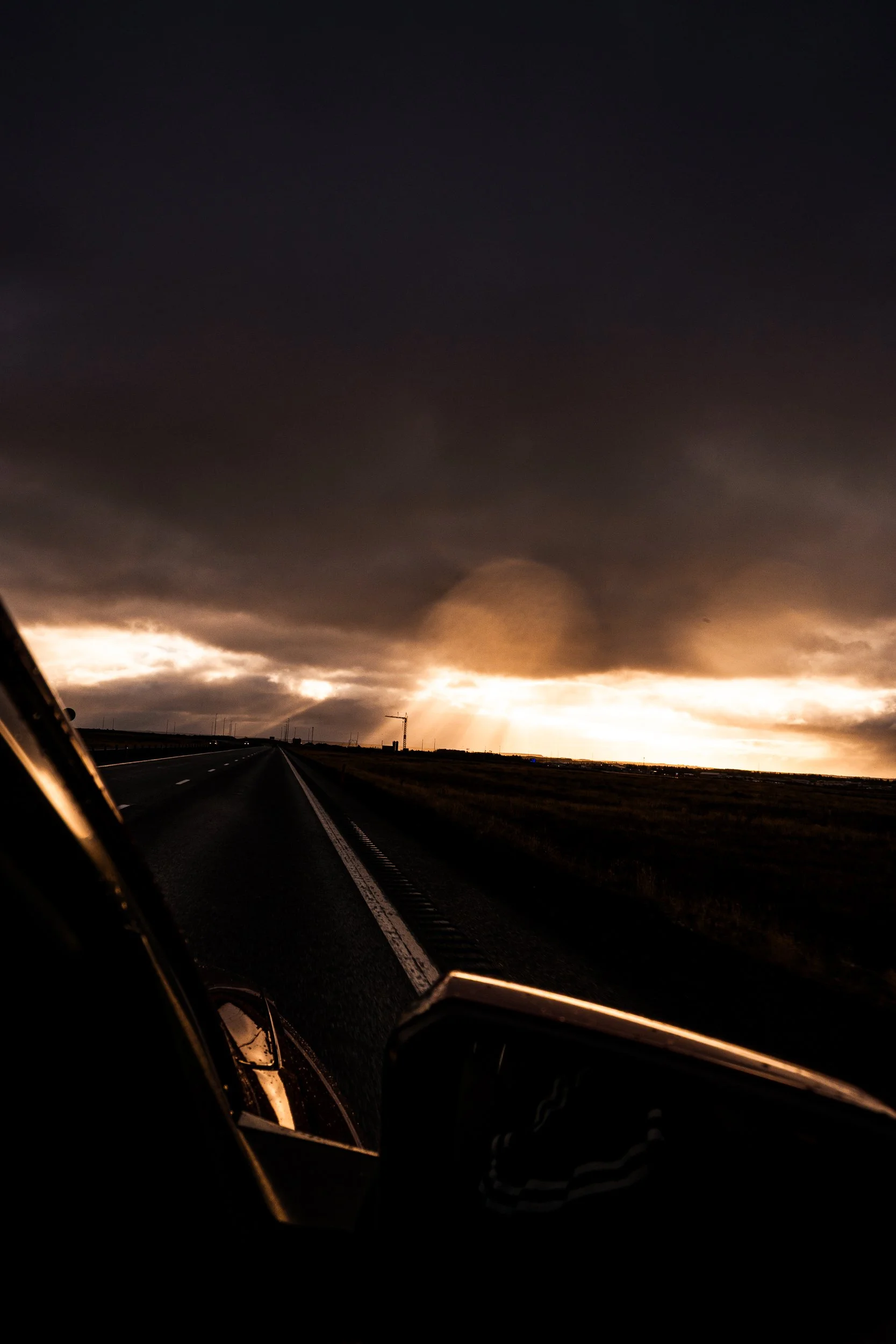Driver’s view of an empty highway beneath dramatic storm clouds and a glowing sunset