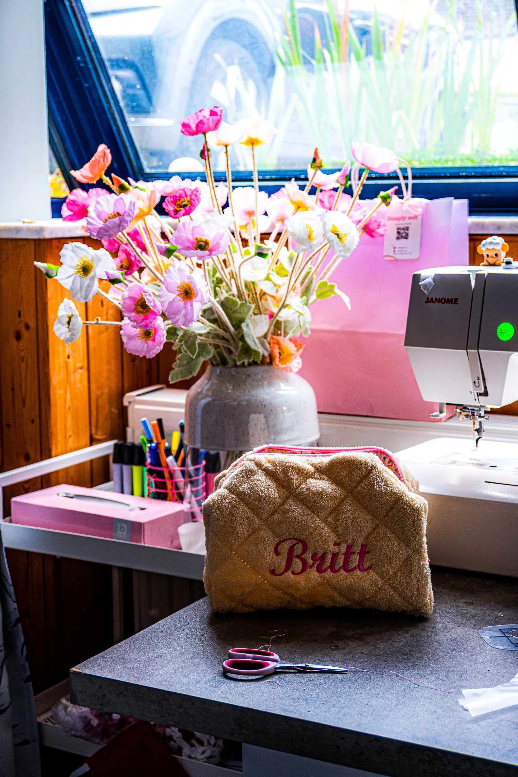 Colorful flower bouquet in a vase beside a Janome sewing machine on a craft table