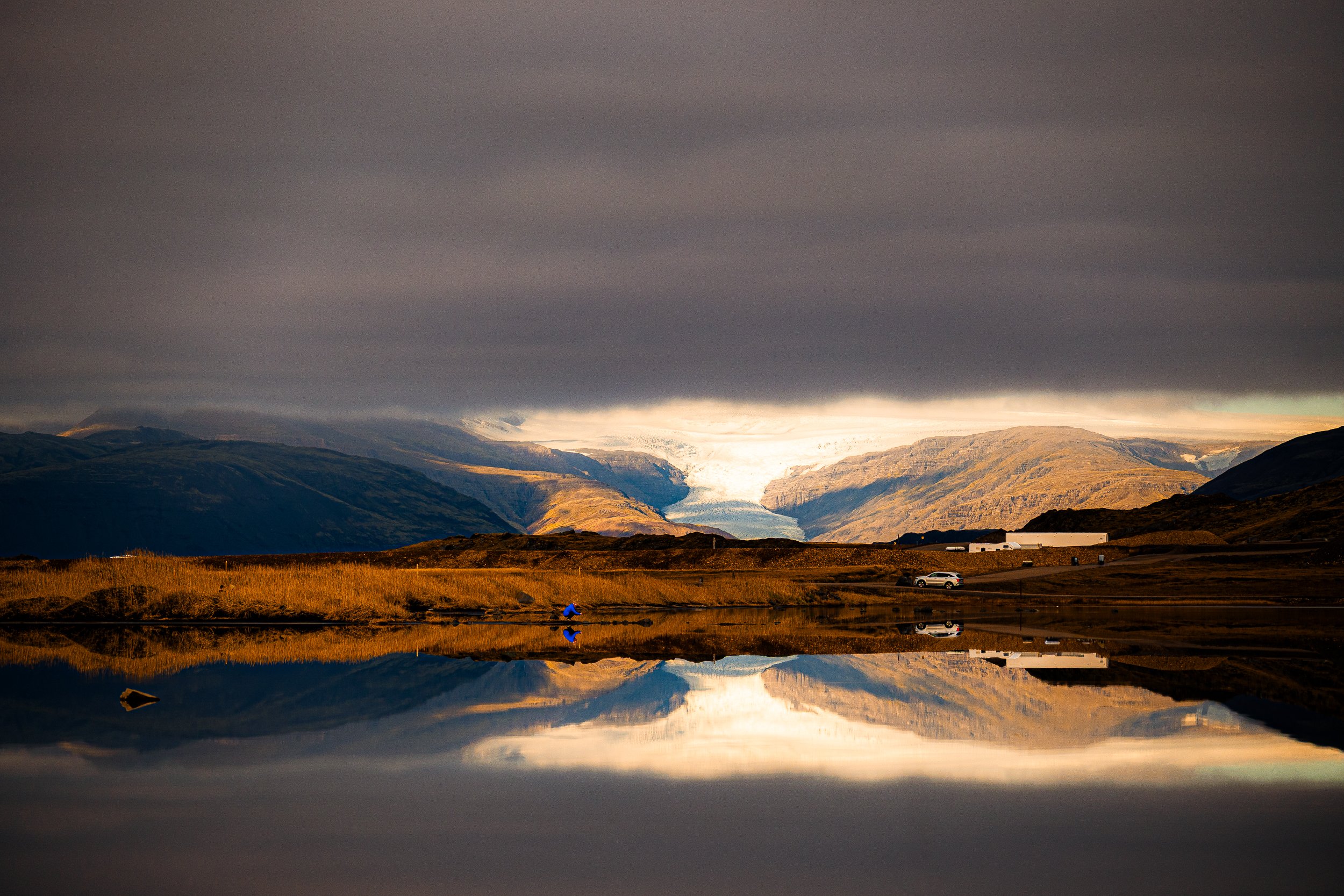Glacier-filled mountain valley under dark storm clouds, reflected in a calm alpine lake
