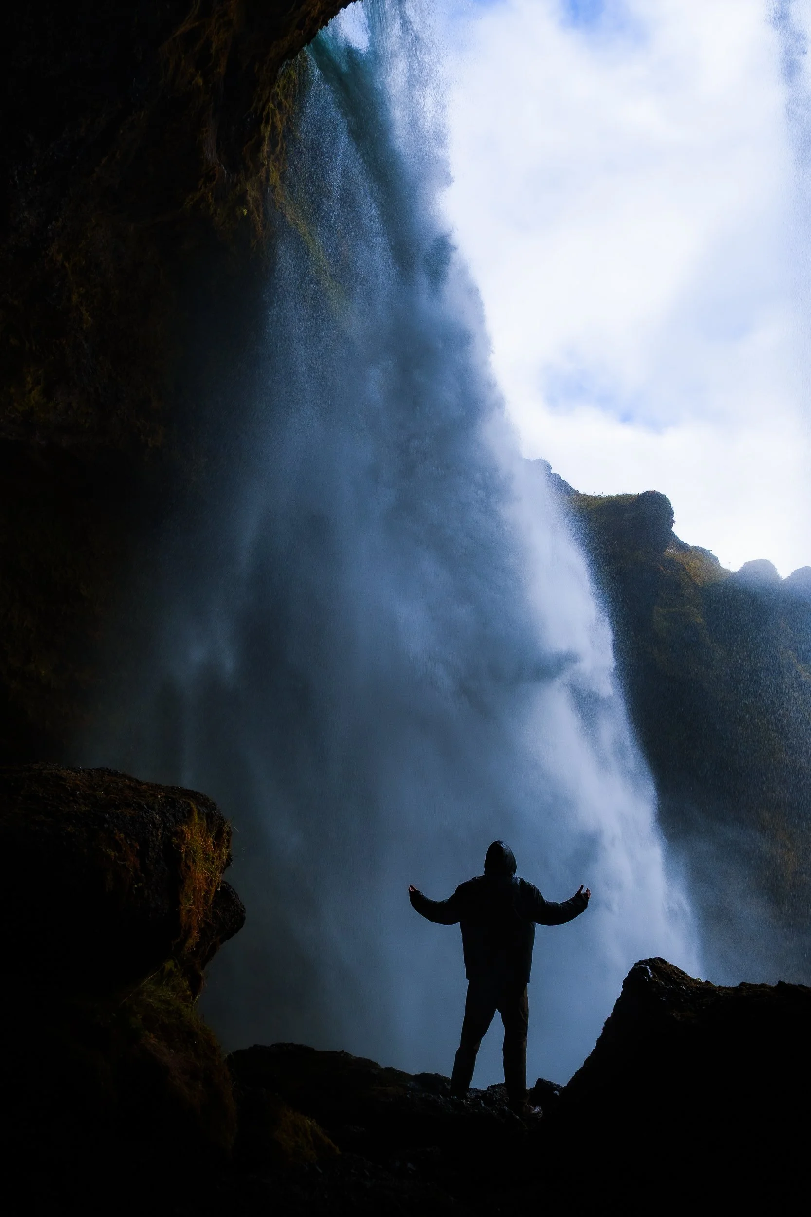 Silhouetted person standing beneath a powerful waterfall in a rocky mountain canyon