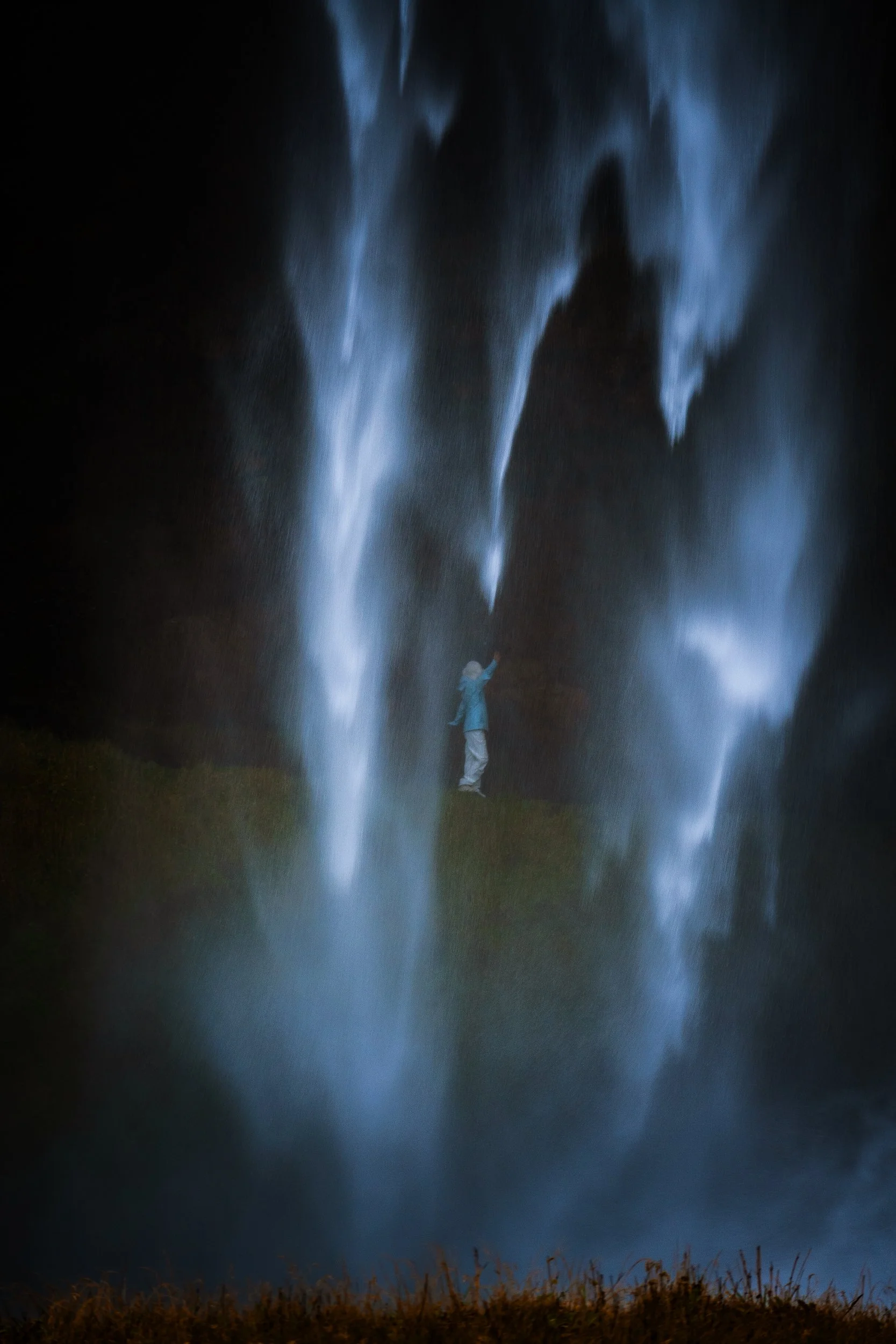 Person standing in a dark field beneath dramatic blue light beams
