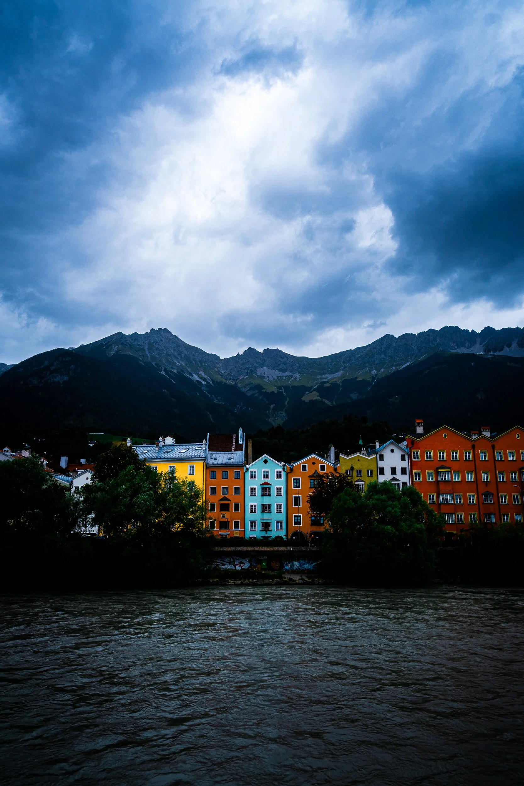 Colorful riverside houses beneath rugged mountains and dramatic clouds
