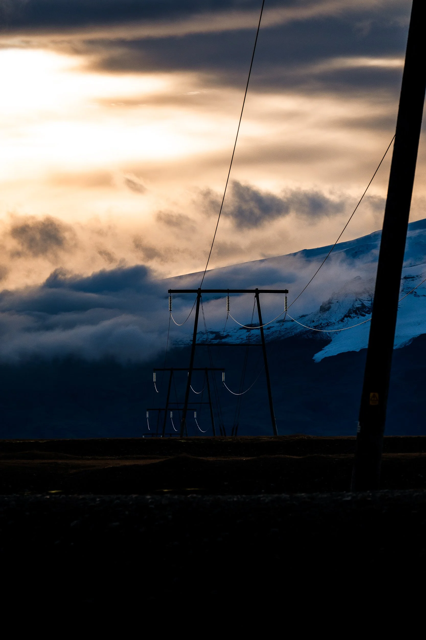Power lines silhouetted against a dramatic sunset over a snow-covered mountain