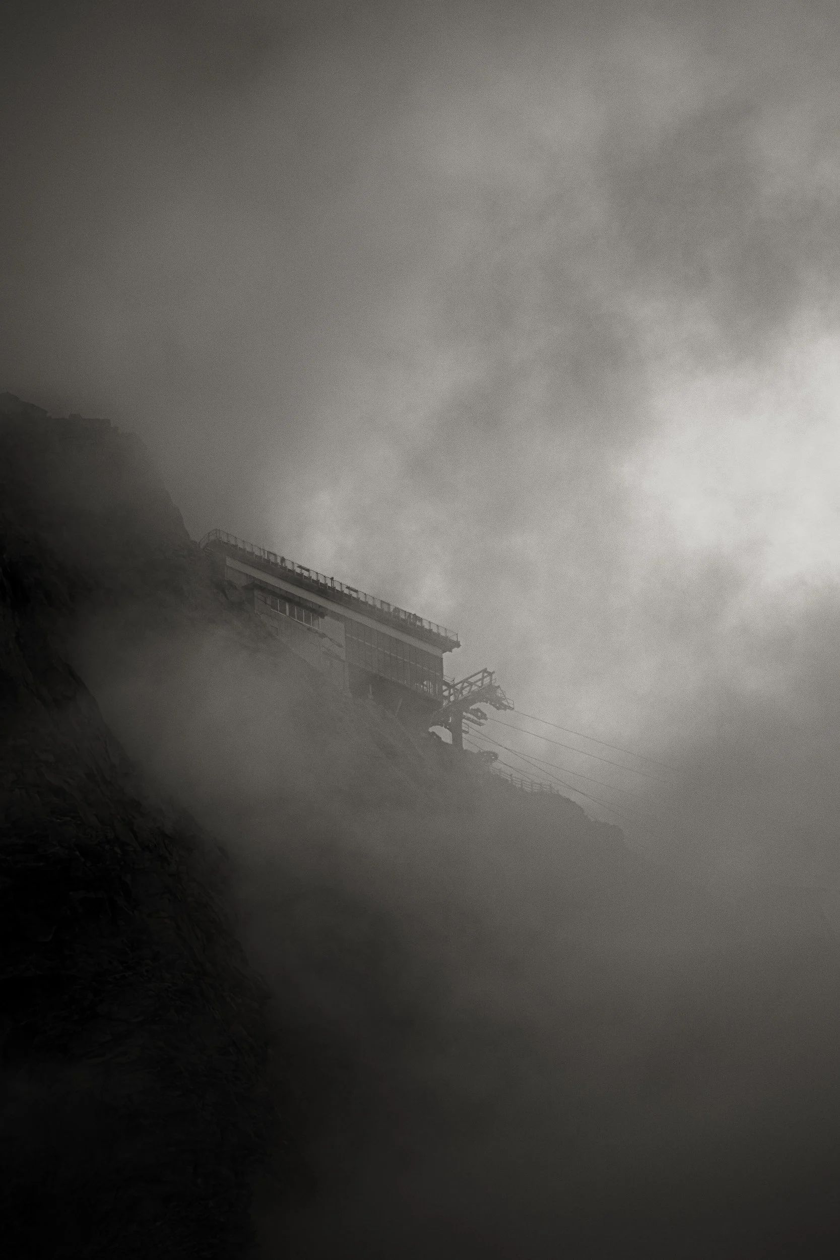 Cable car station on a steep rocky mountain enveloped in dense fog
