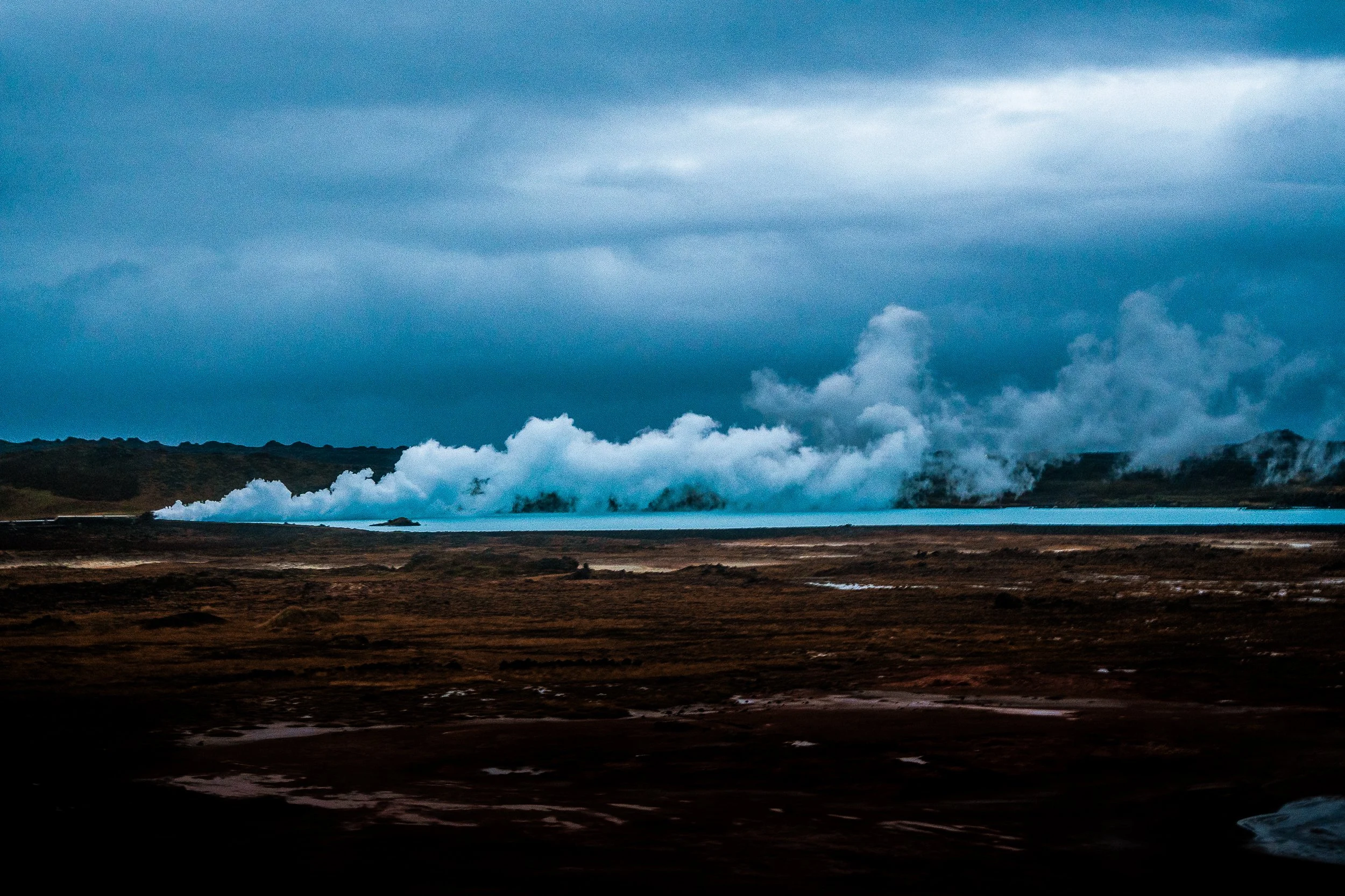 Blue geothermal lagoon steaming beneath a cloudy sky in a dark volcanic landscape