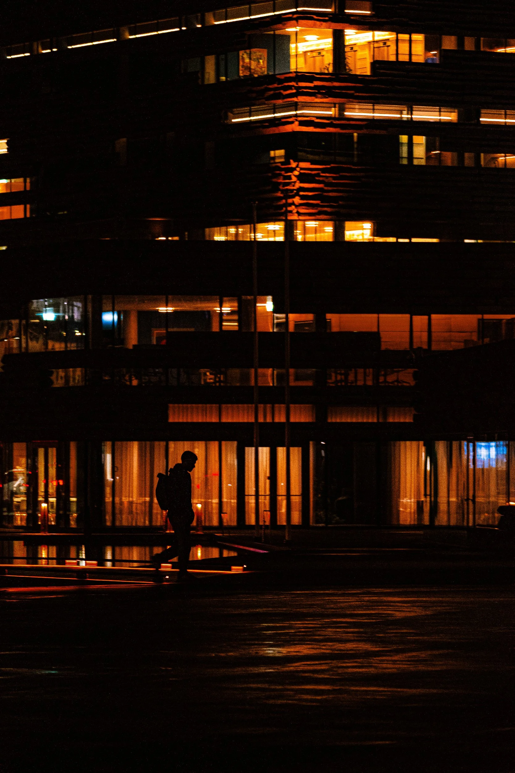 Silhouetted person walking past a modern office building glowing with warm lights at night