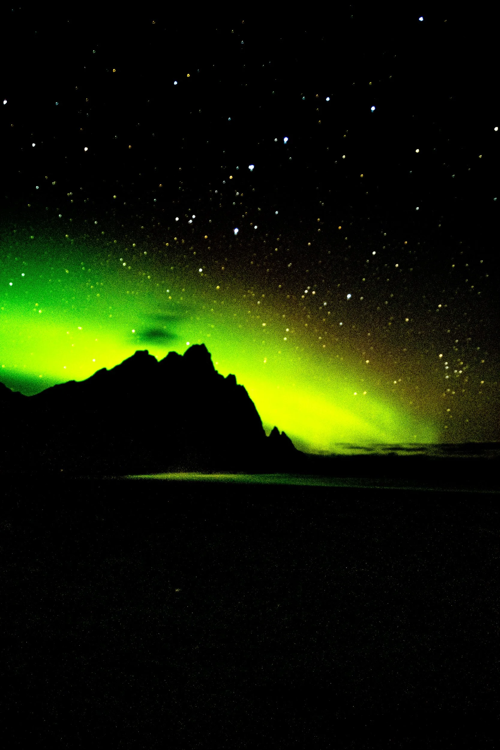 Jagged mountain silhouette beneath a vivid green aurora and star-filled night sky