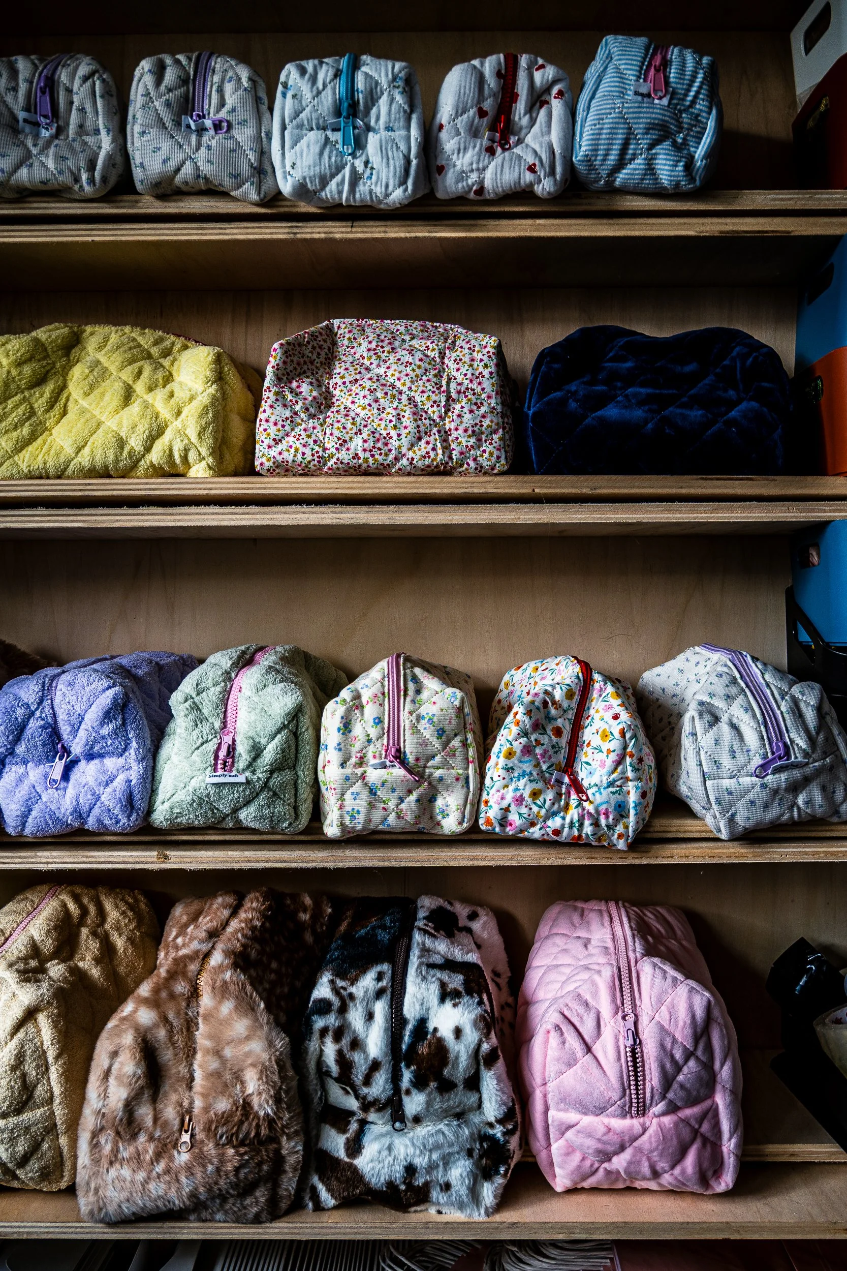 Shelves stocked with colorful quilted and fleece zippered pouches in floral, striped, heart, and animal-print patterns.