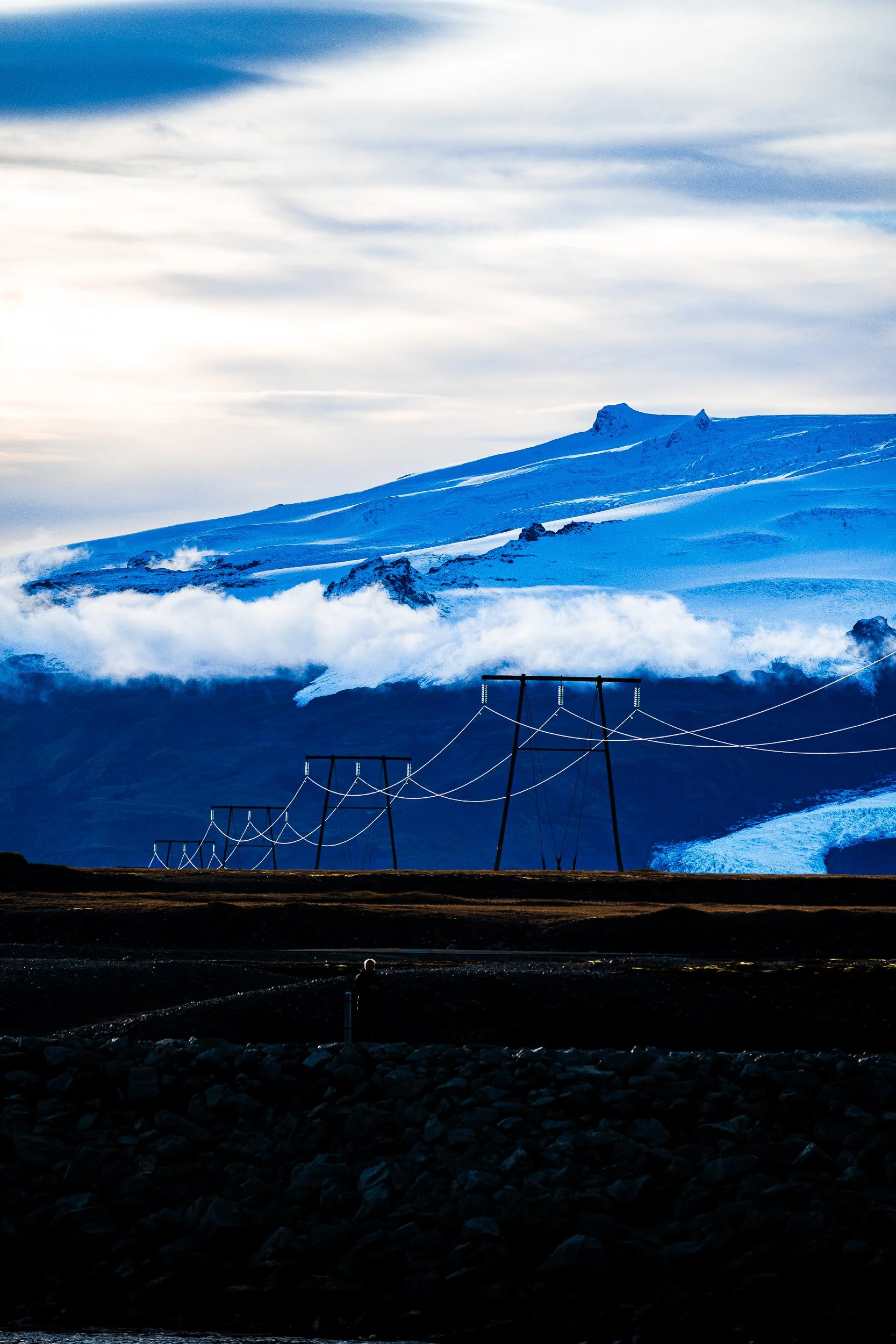 Snow-covered volcanic mountain rising above clouds with power lines in the foreground