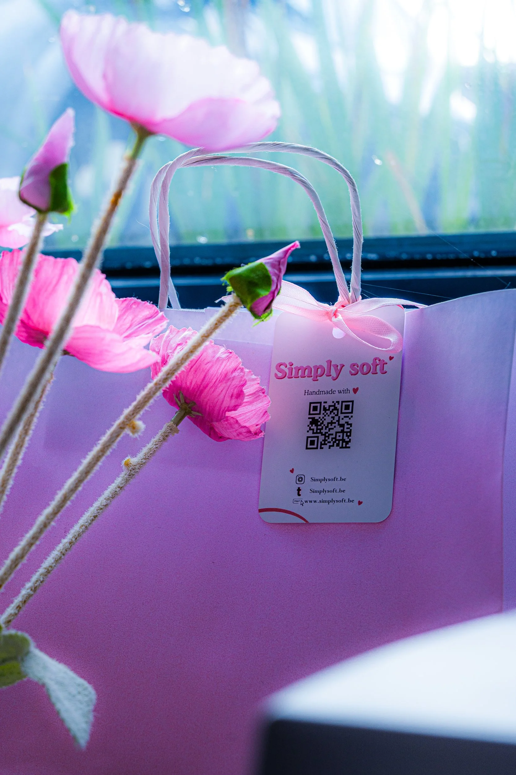 Pink handmade gift bag with ribbon handles, pink flowers, and a “Simply soft” product tag with QR code