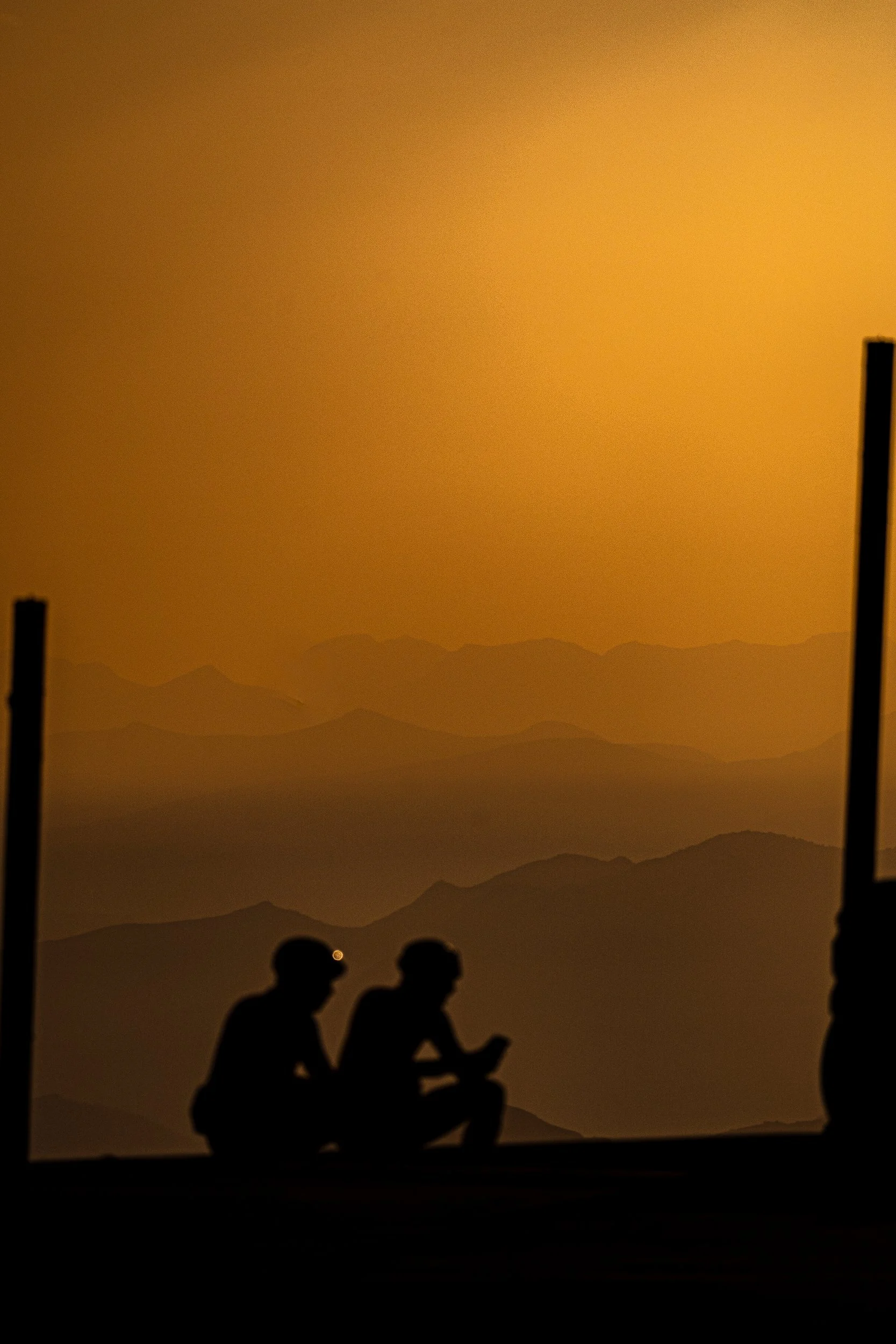 Silhouettes of two people sitting before a glowing mountain landscape scene.