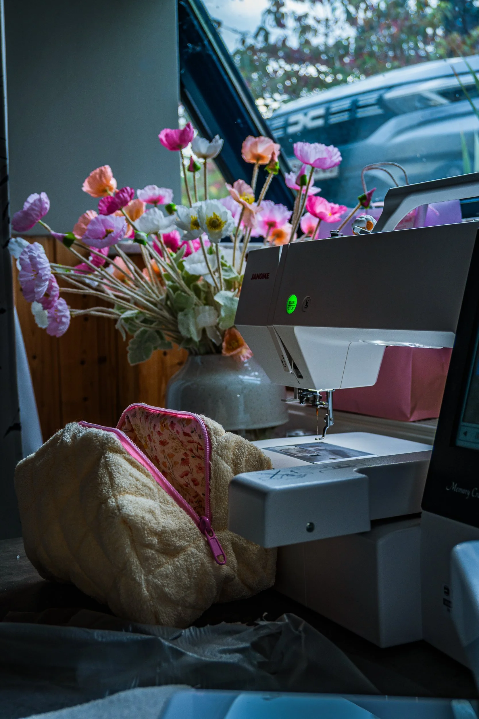 Janome sewing machine beside a vase of colorful flowers and a fabric sewing project by a window