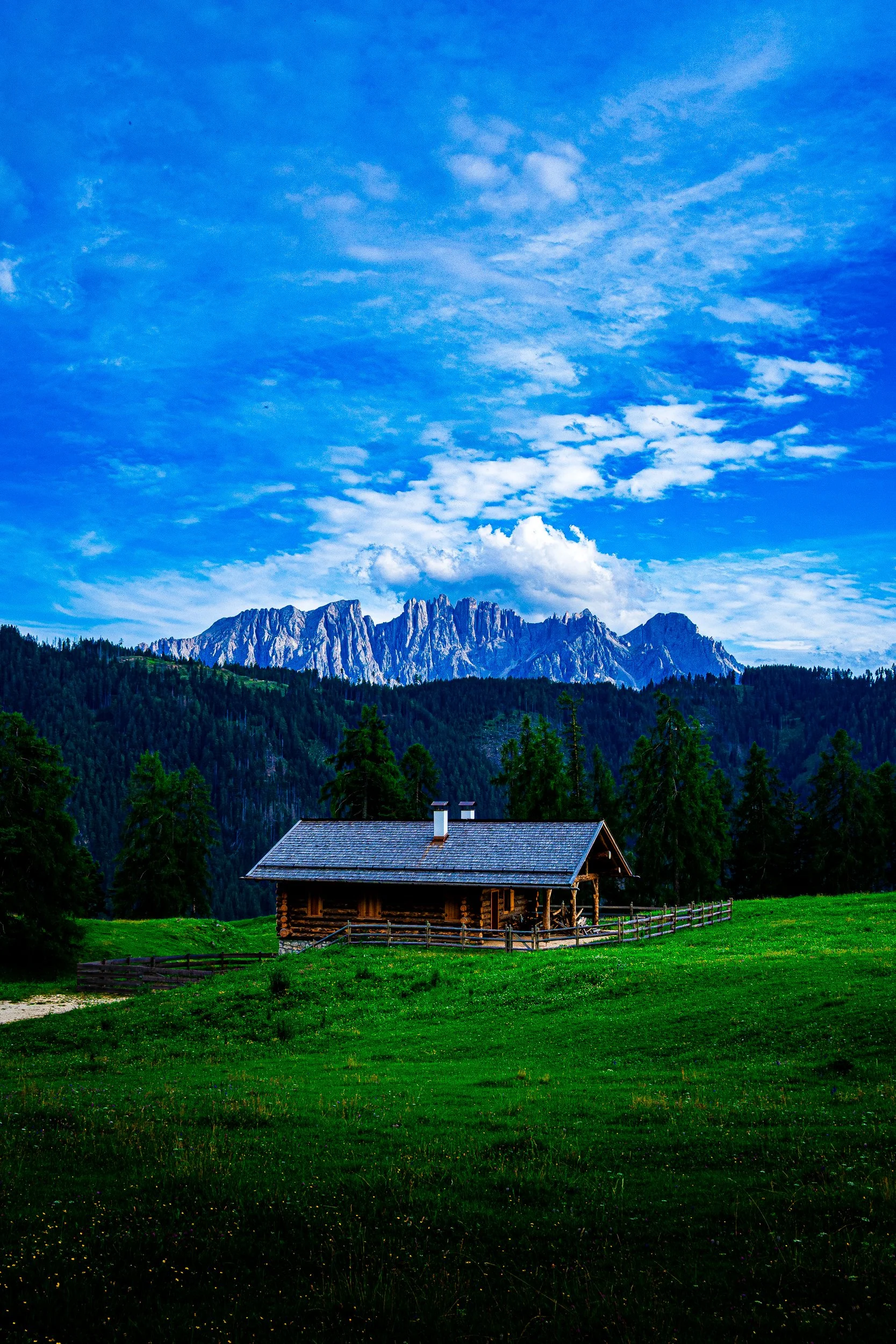 Rustic log cabin in a green alpine meadow beneath the jagged Dolomite mountains and blue sky