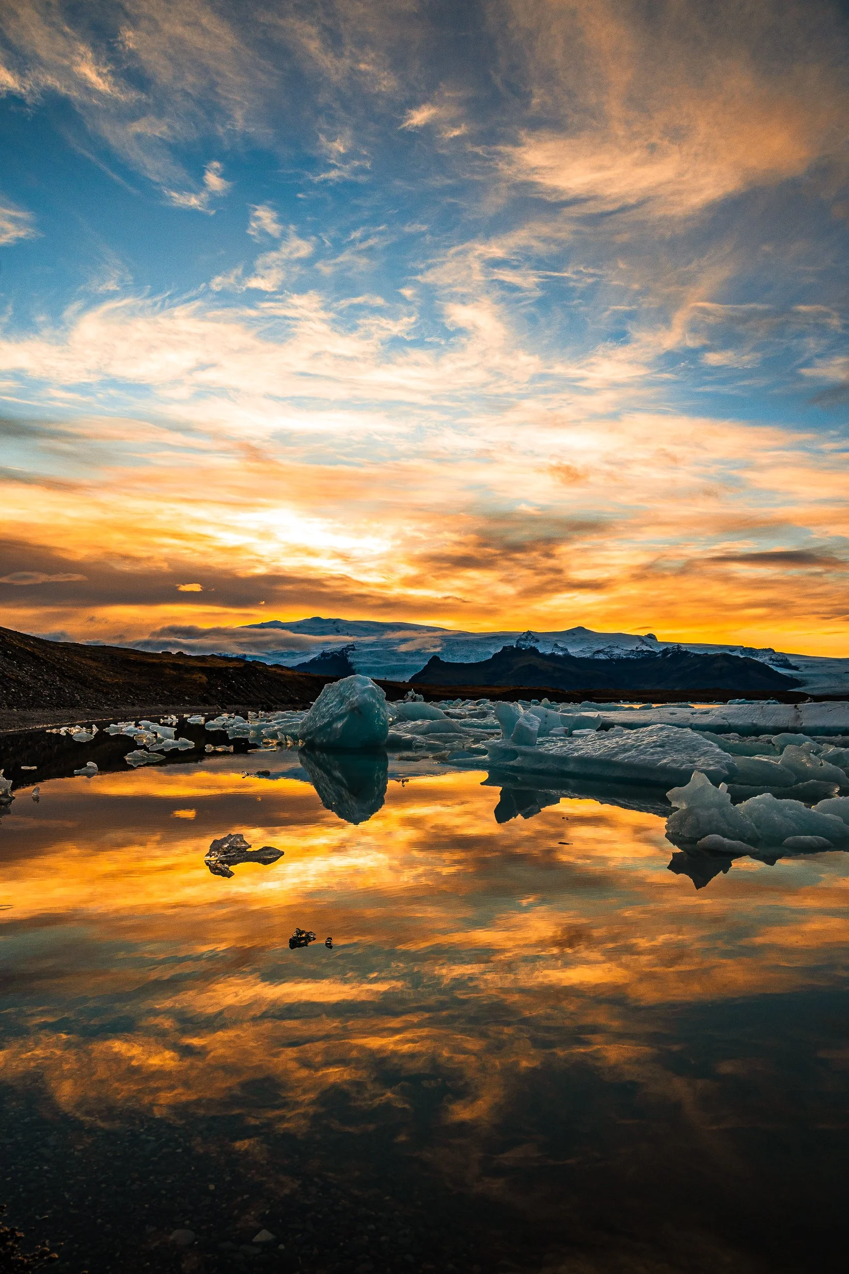 Glacial lagoon with floating icebergs reflecting a vivid orange sunset beneath snow-covered mountains