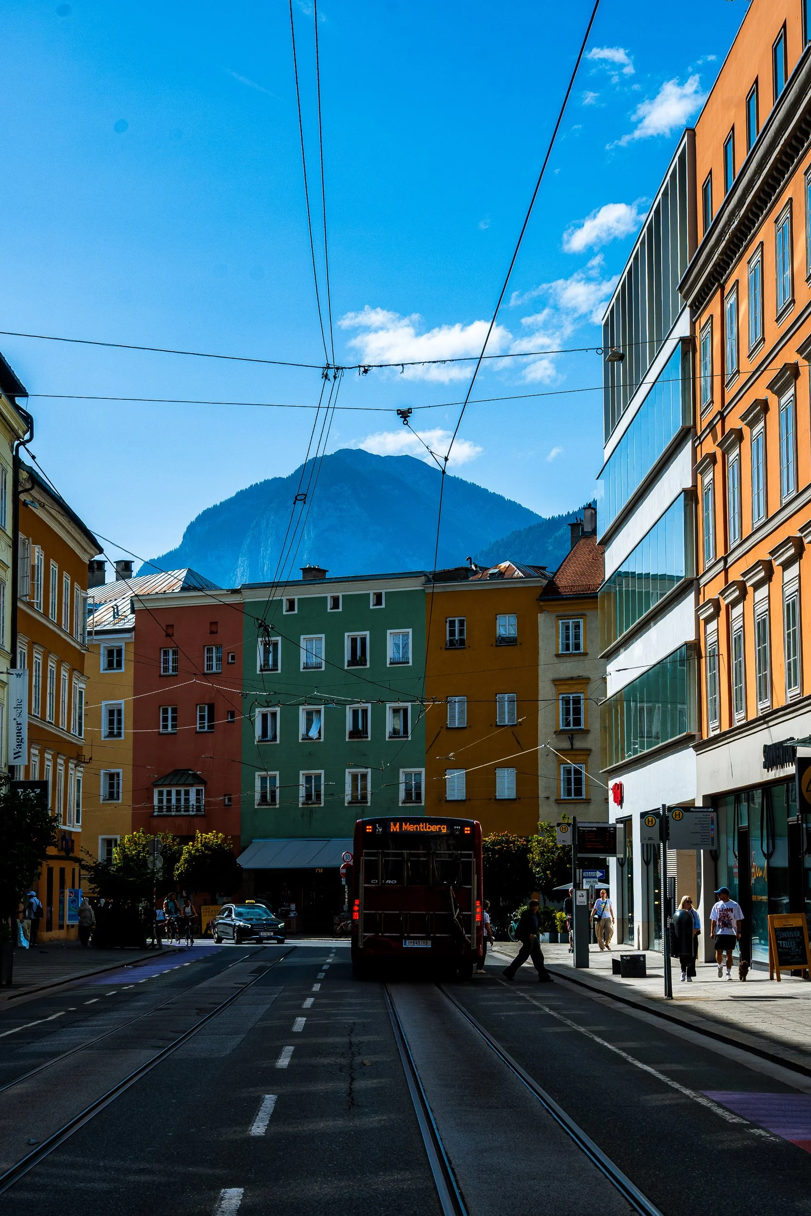 City street with a bus, tram tracks, colorful buildings, overhead wires, and a mountain backdrop in Bad Ischl, Austria
