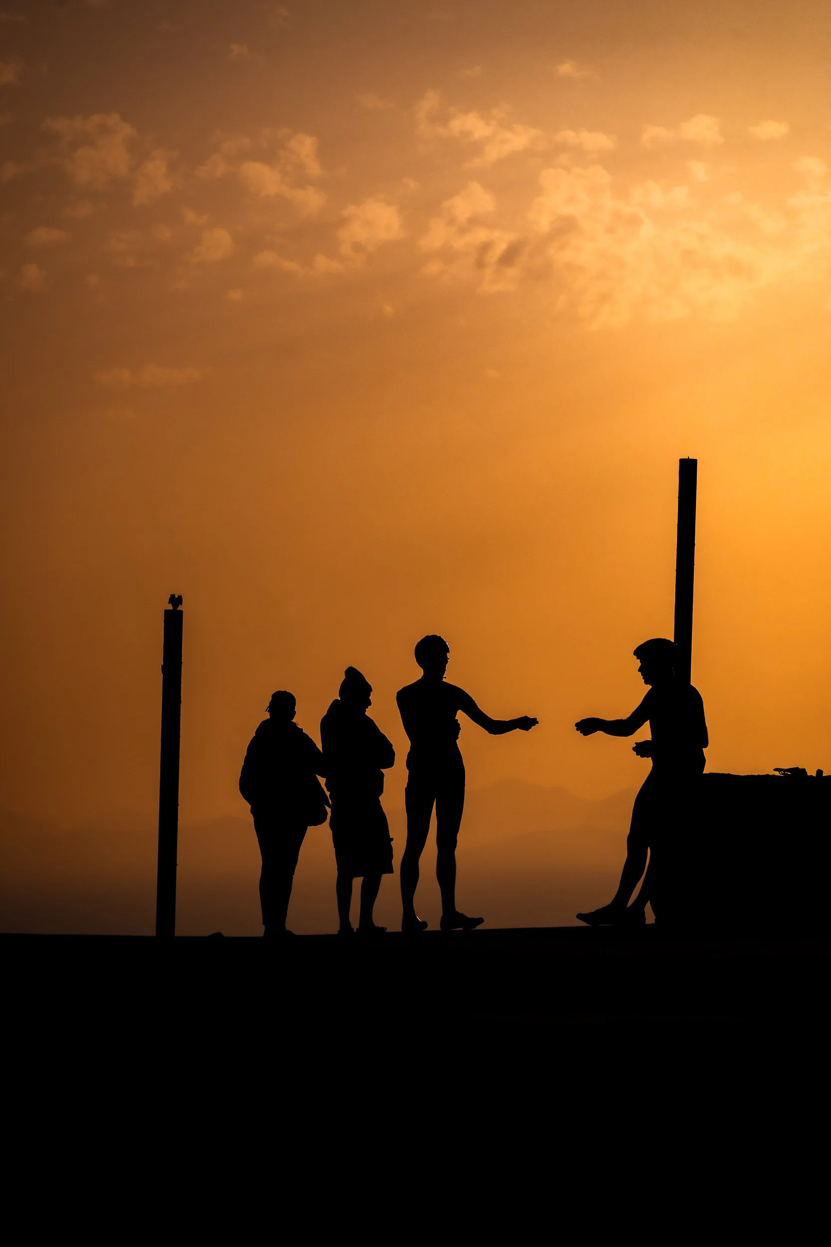 Silhouettes of four people talking against a dramatic orange sunset sky