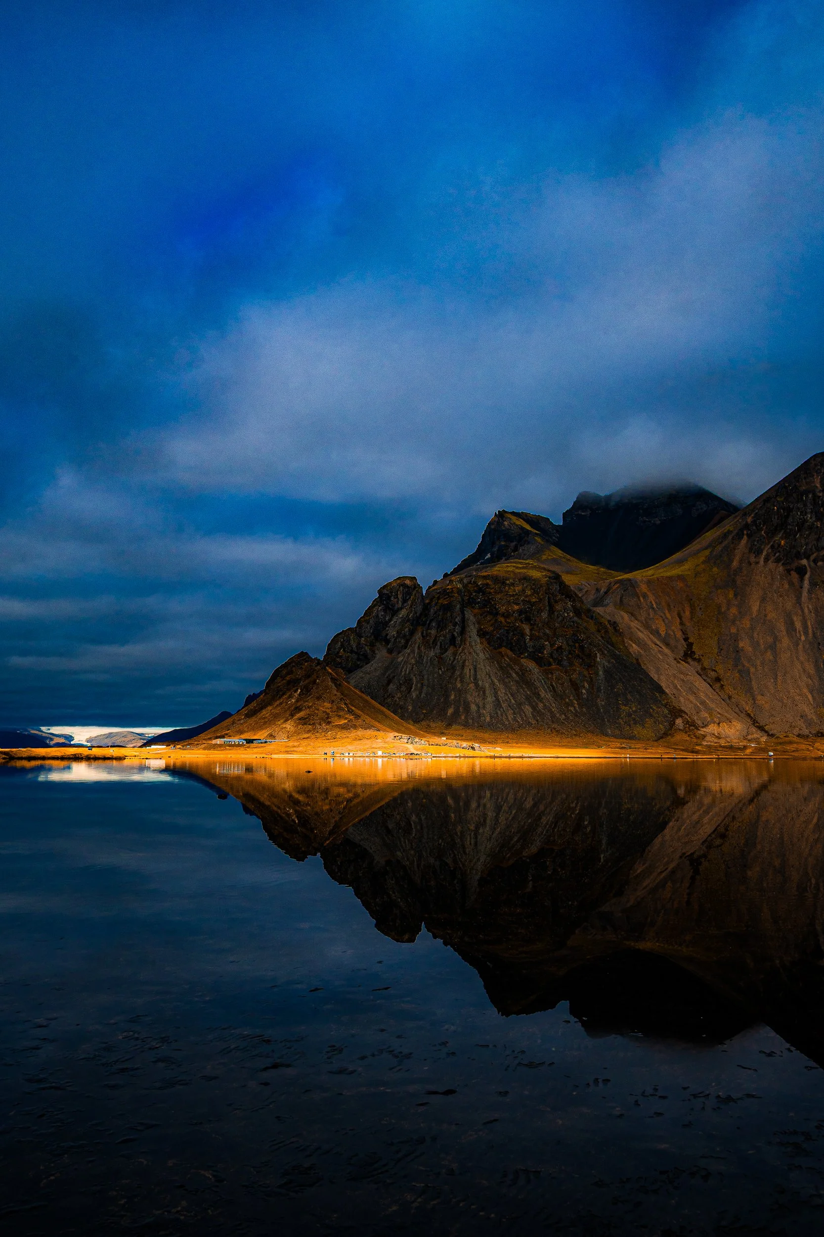 Dramatic mountain landscape reflected in a calm lake beneath a blue, cloud-filled sky