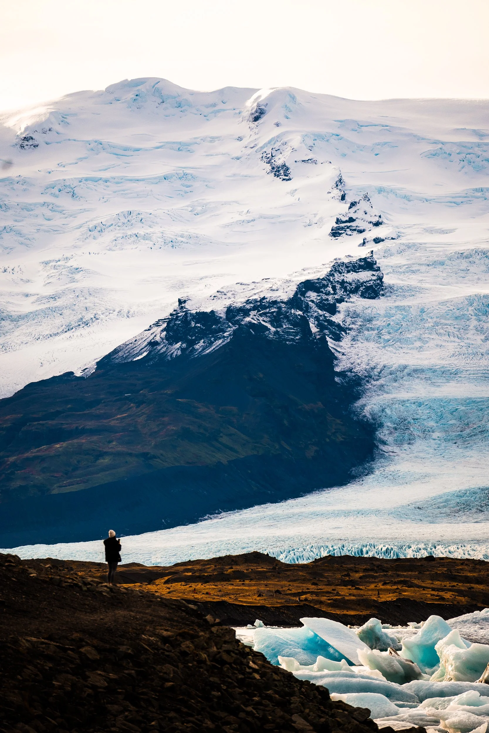 Person viewing a rugged, snow-covered volcanic mountain and glacier in Iceland