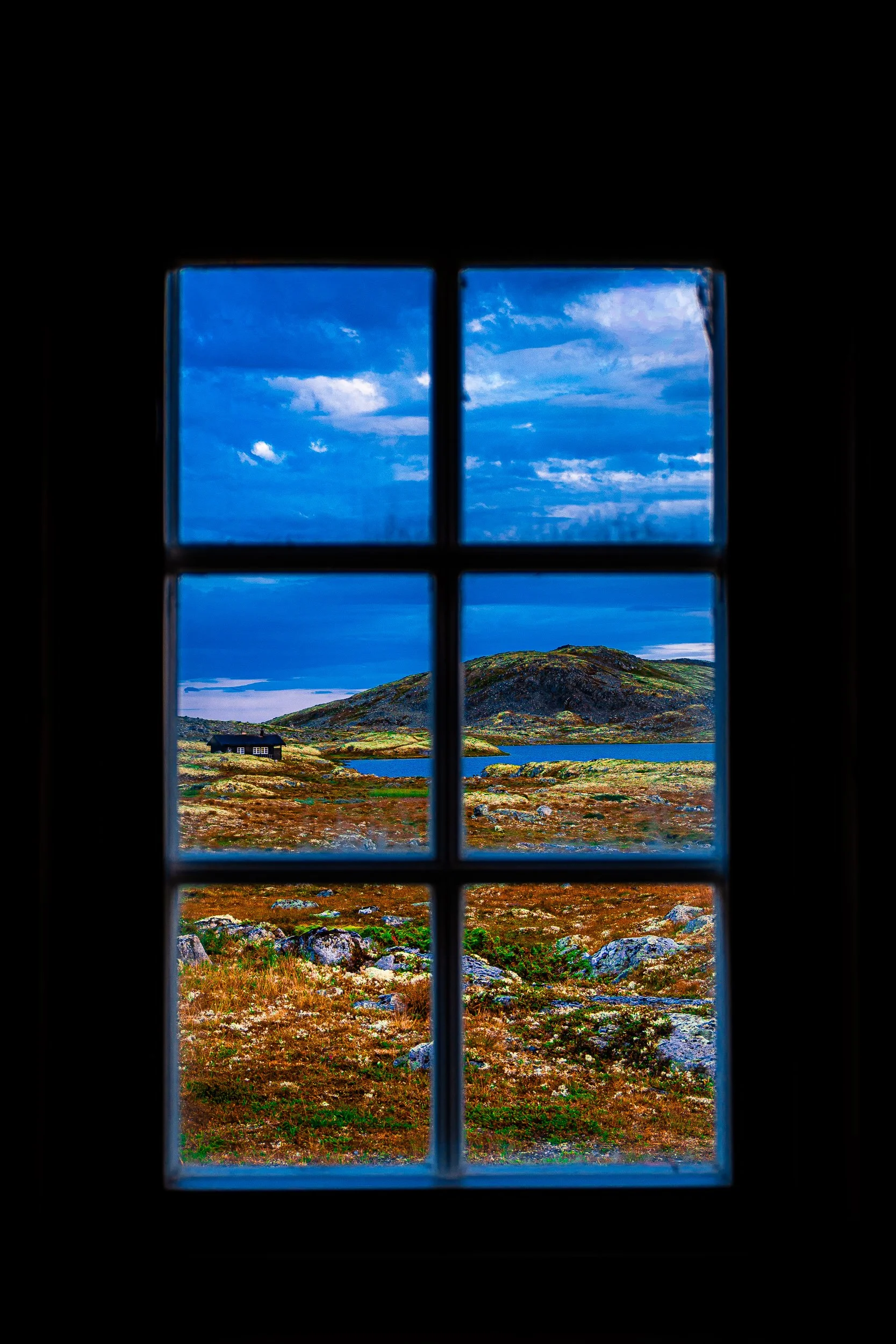 Mountain landscape with a lakeside cabin viewed through a six-pane window