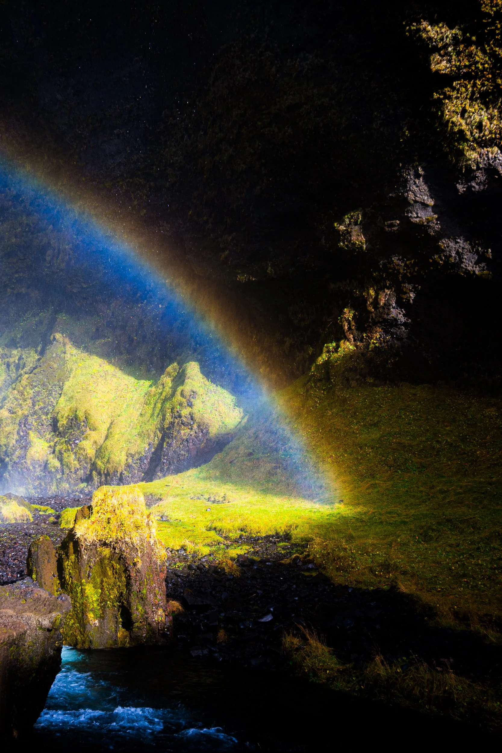 Rainbow over a moss-covered waterfall and rocky stream in a dark forest