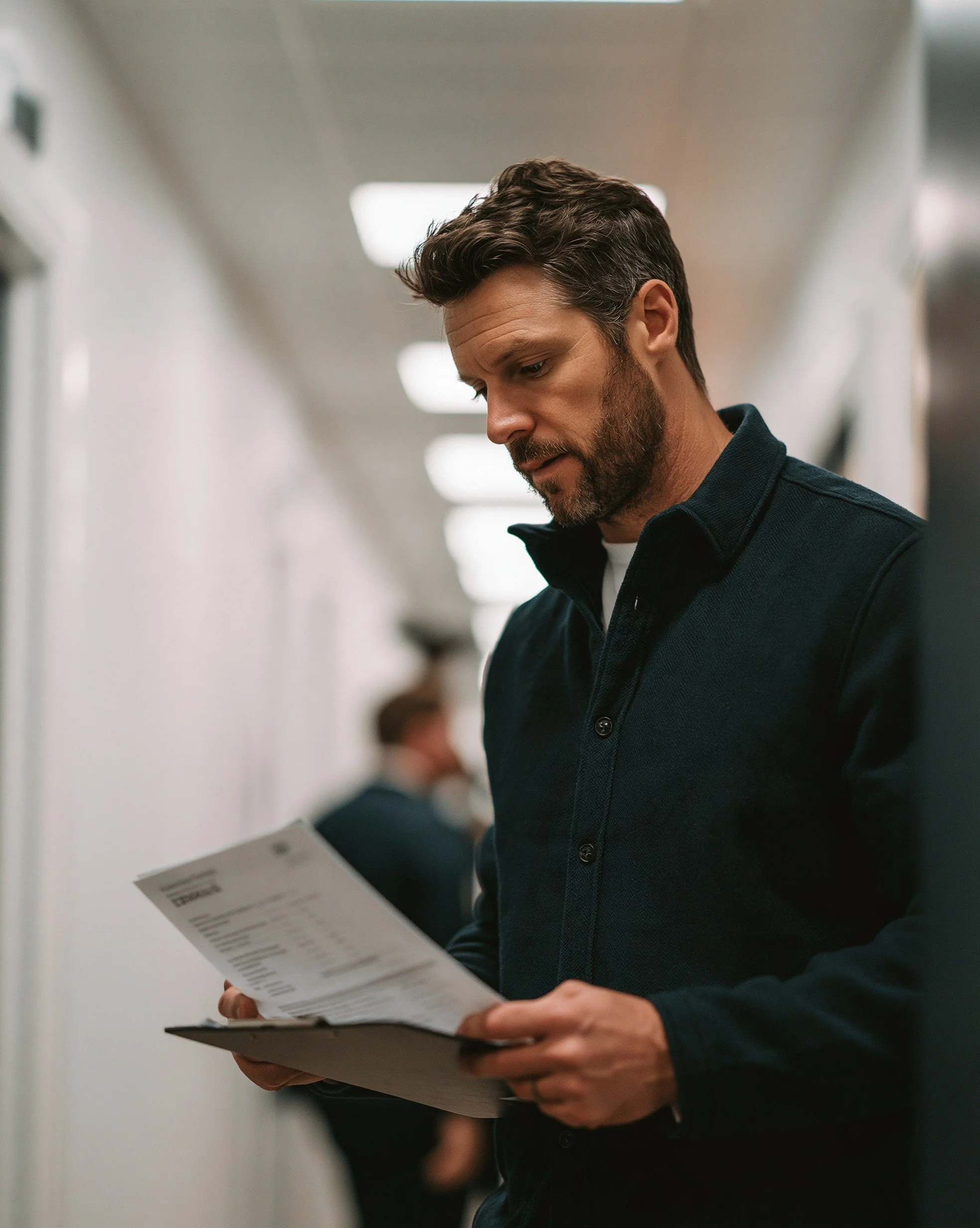 A facilities manager reviewing a printed MEES compliance report on a clipboard in a modern clinical corridor.
