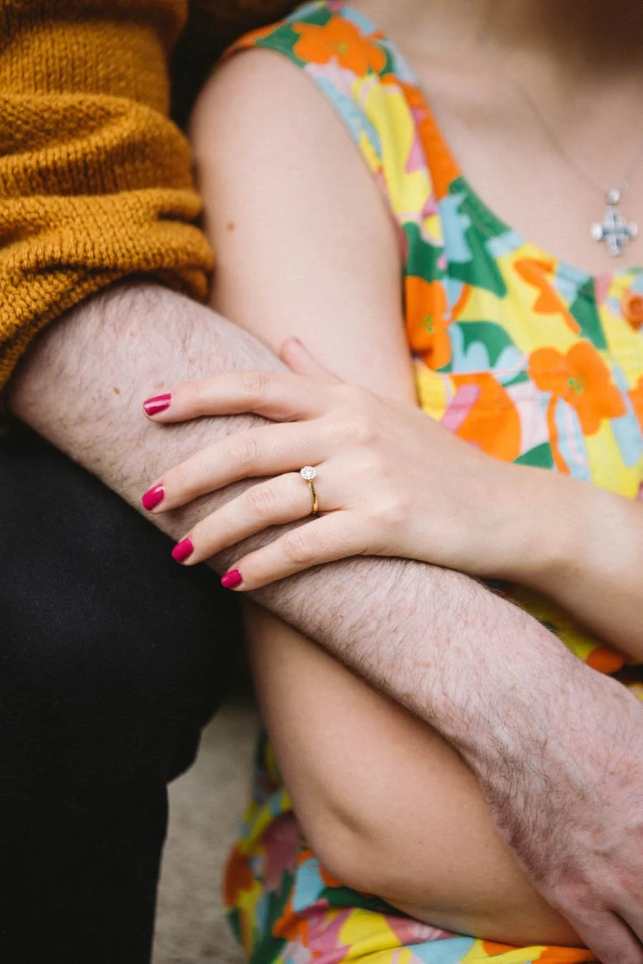 Close up of an engagement ring as couple lean against each other, man's arms wrapped around his fiancée.