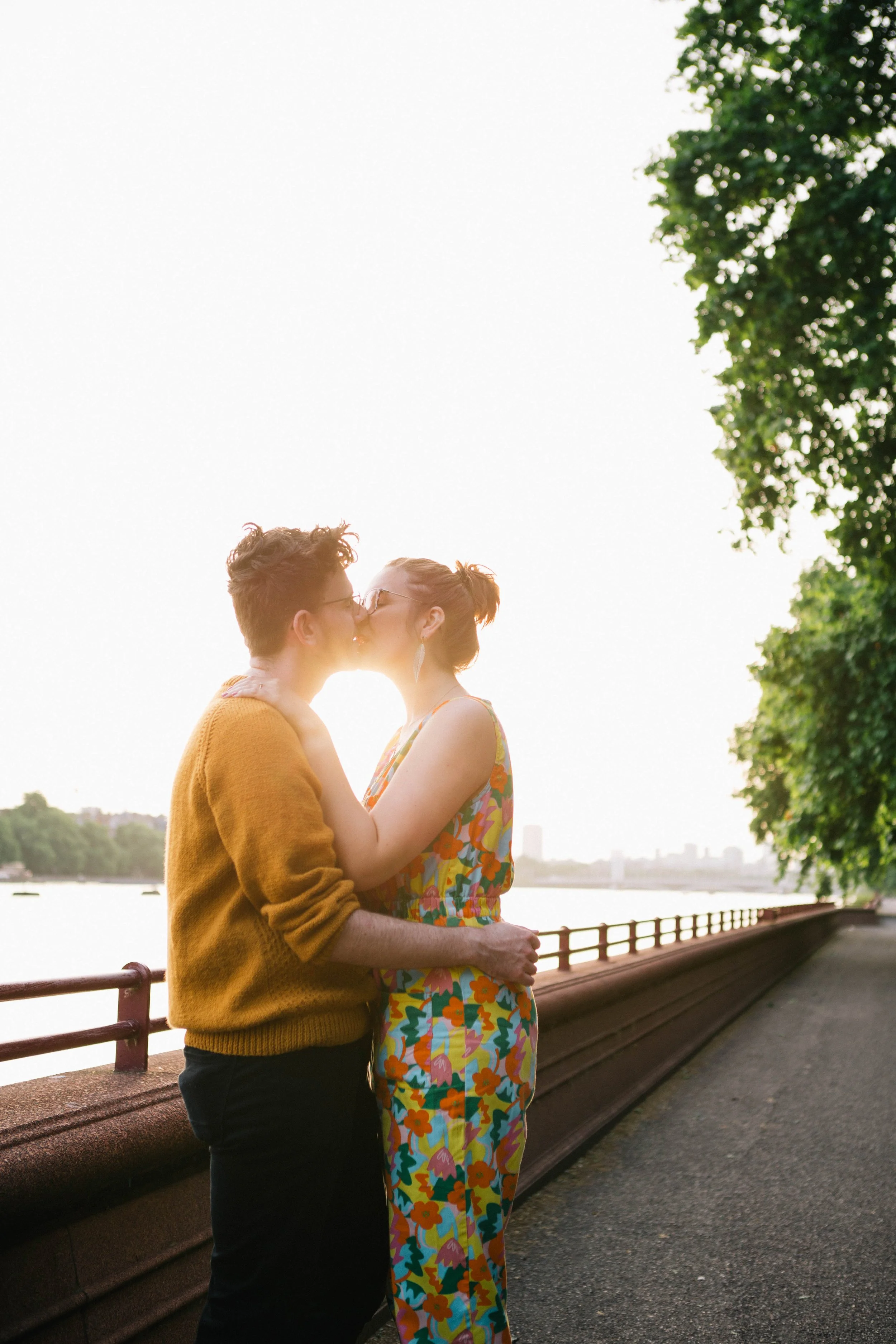 The sun shines between the engaged couple as they kiss during their pre-wedding photography session