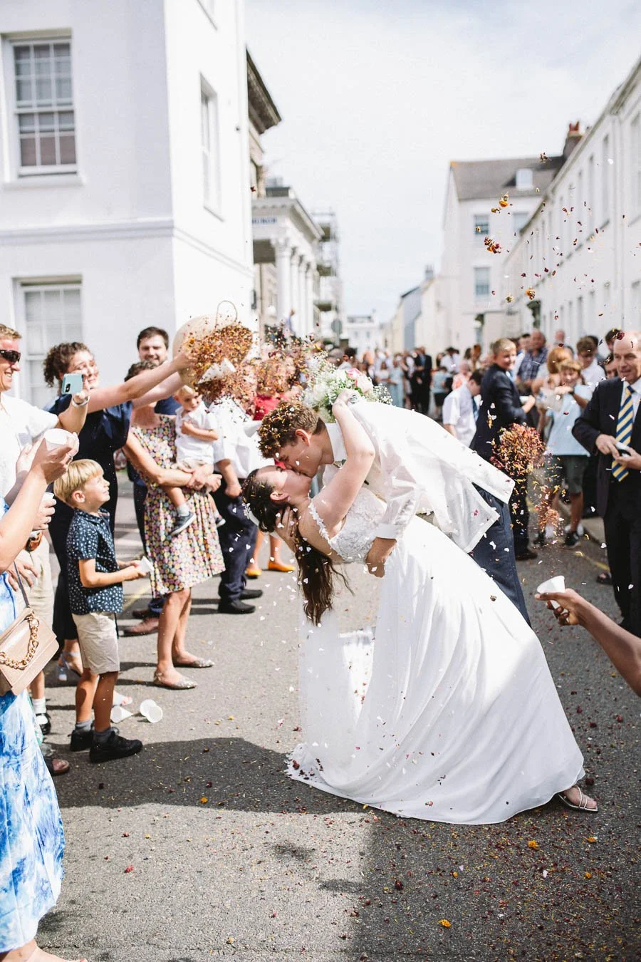 Bride and groom in a dip kiss as their wedding guests throw confetti on them.