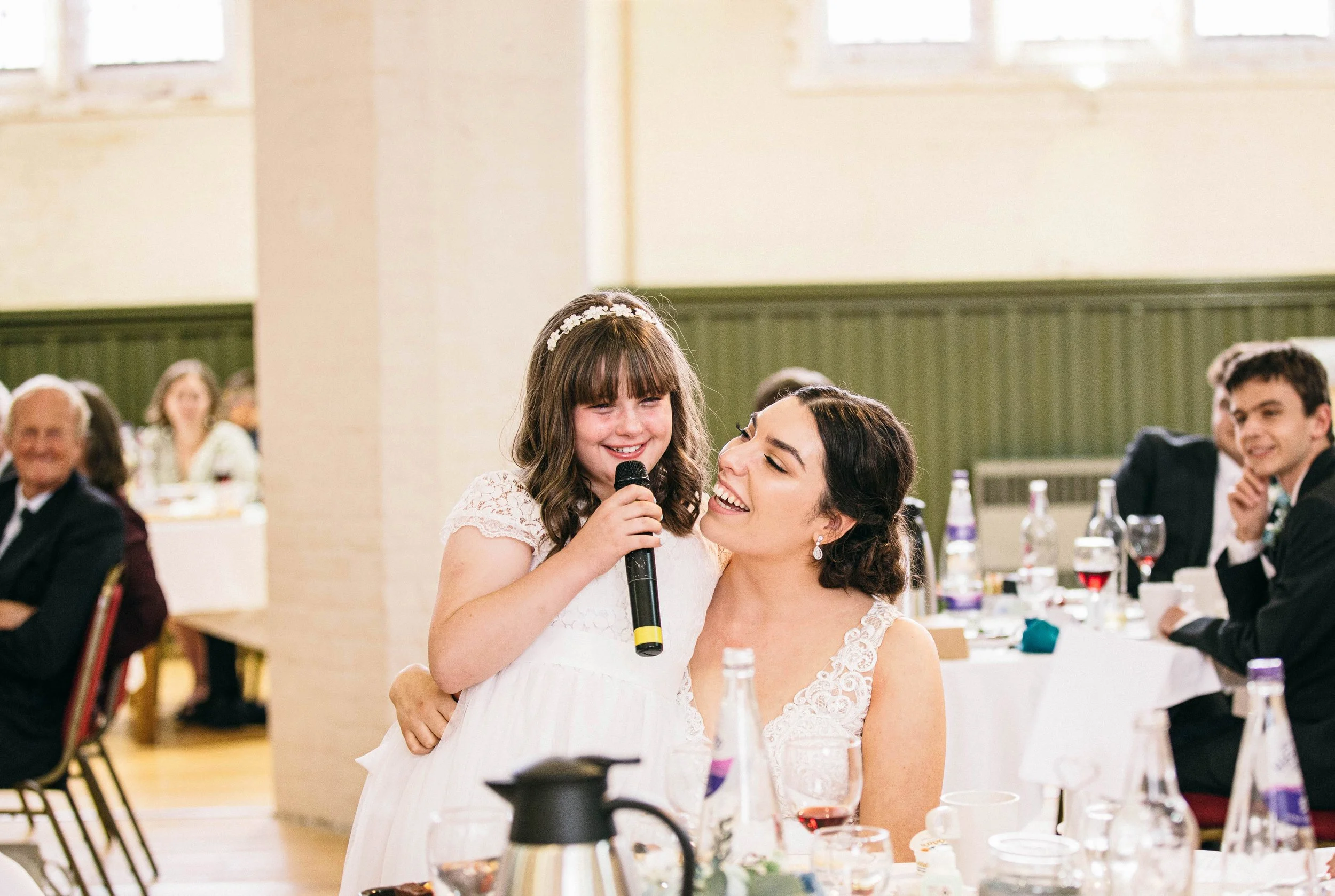 Bride listens to speech from young bridesmaid as they smile at each other