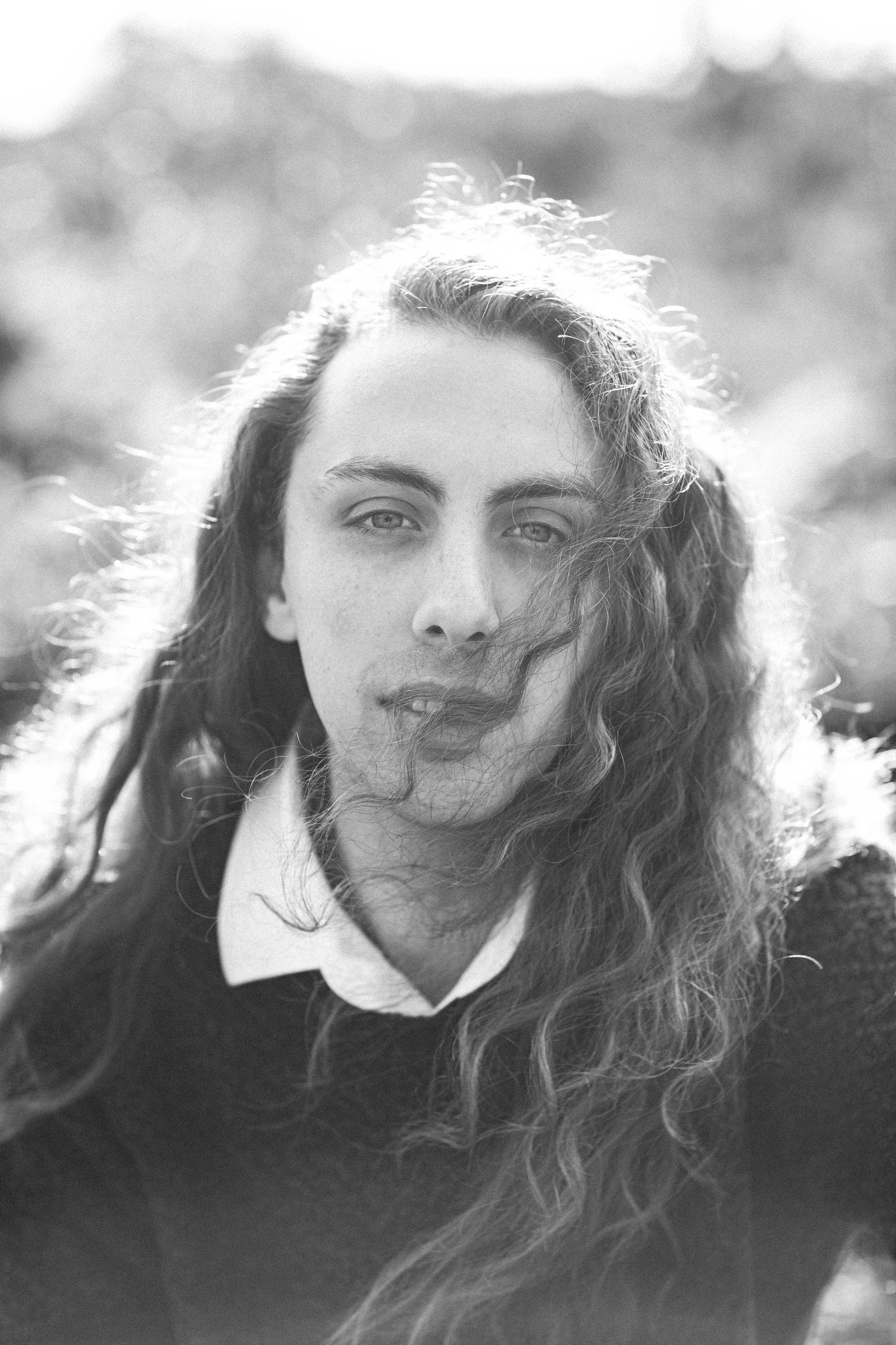Close up black and white image of man with long hair blowing across his face.