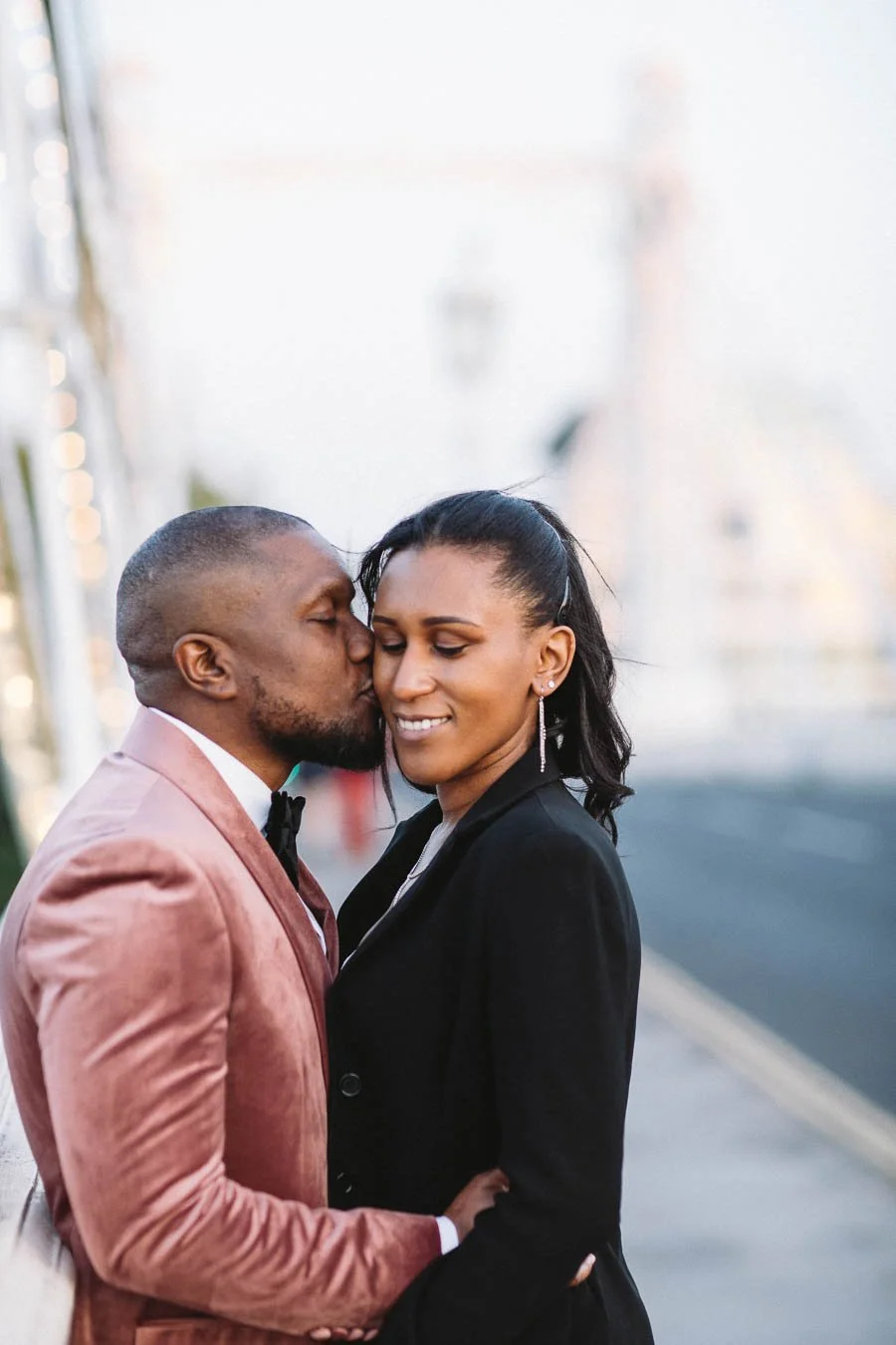 Man kisses his fiancée on the cheek as she smiles on the Prince Albert Bridge.