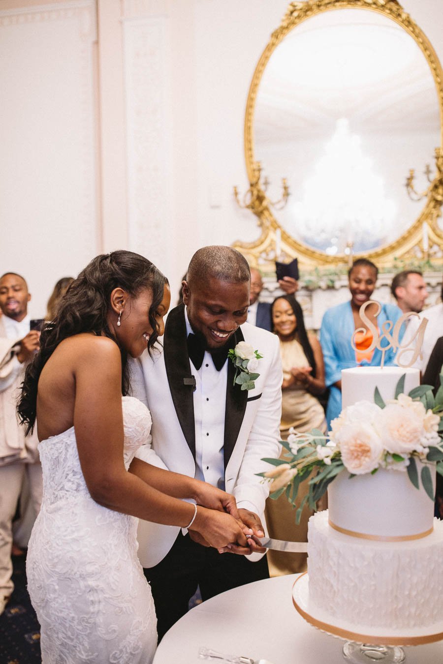 Bride and groom cut the cake at their wedding reception in Grove House. Their family and friends watch in the background.
