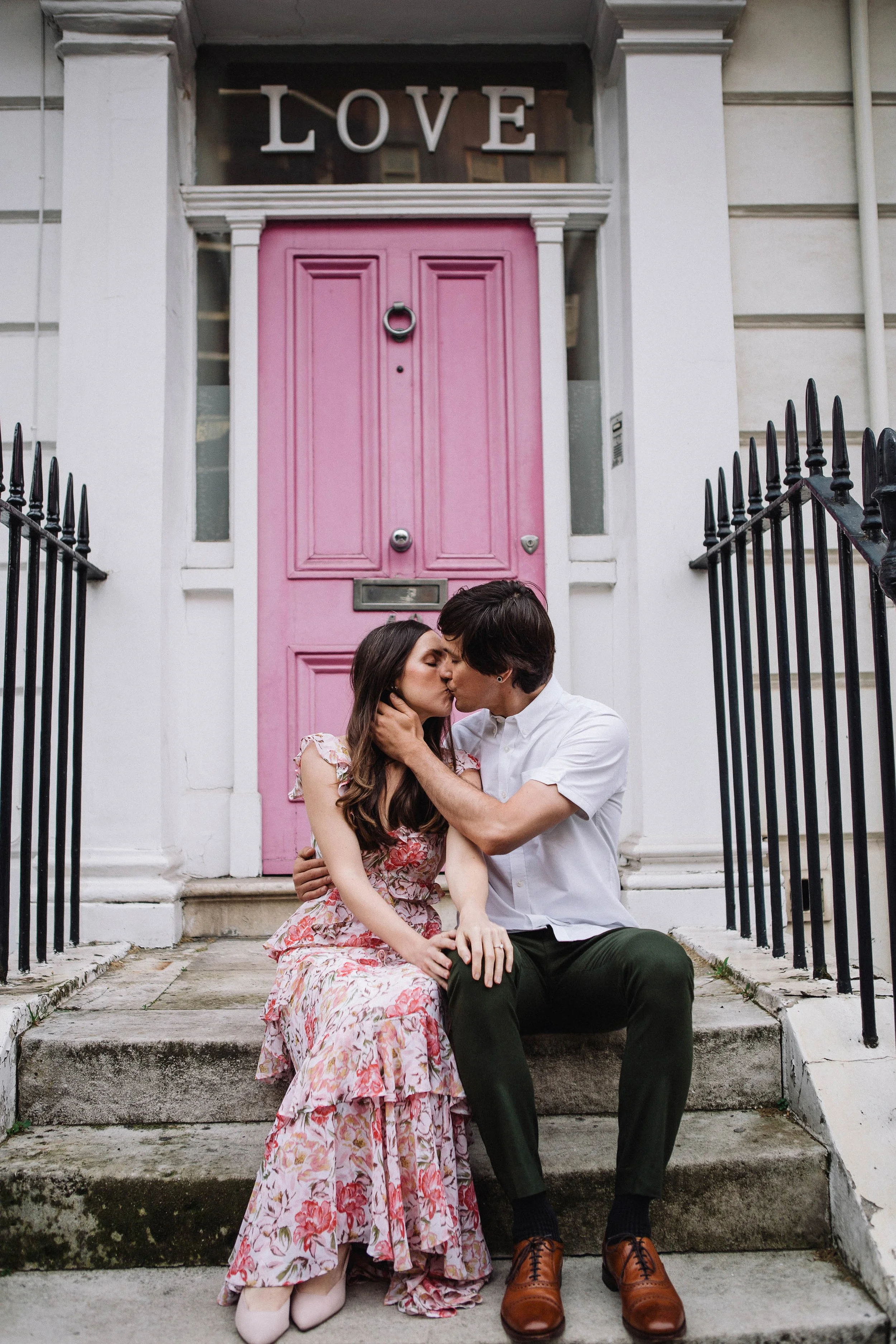 Couple kiss in front of a pink door during their pre-wedding photography session