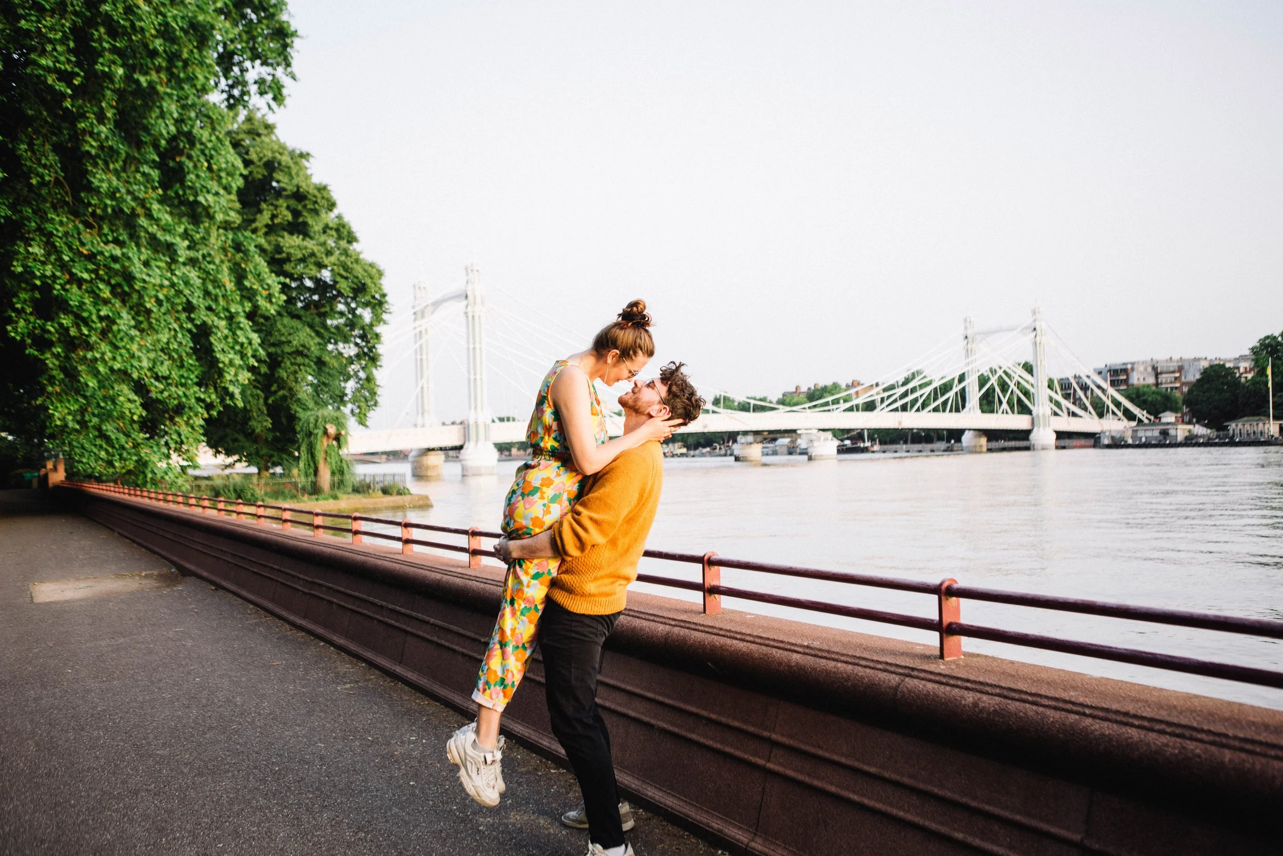 Couple embracing by the River Thames with London's Albert Bridge in the background