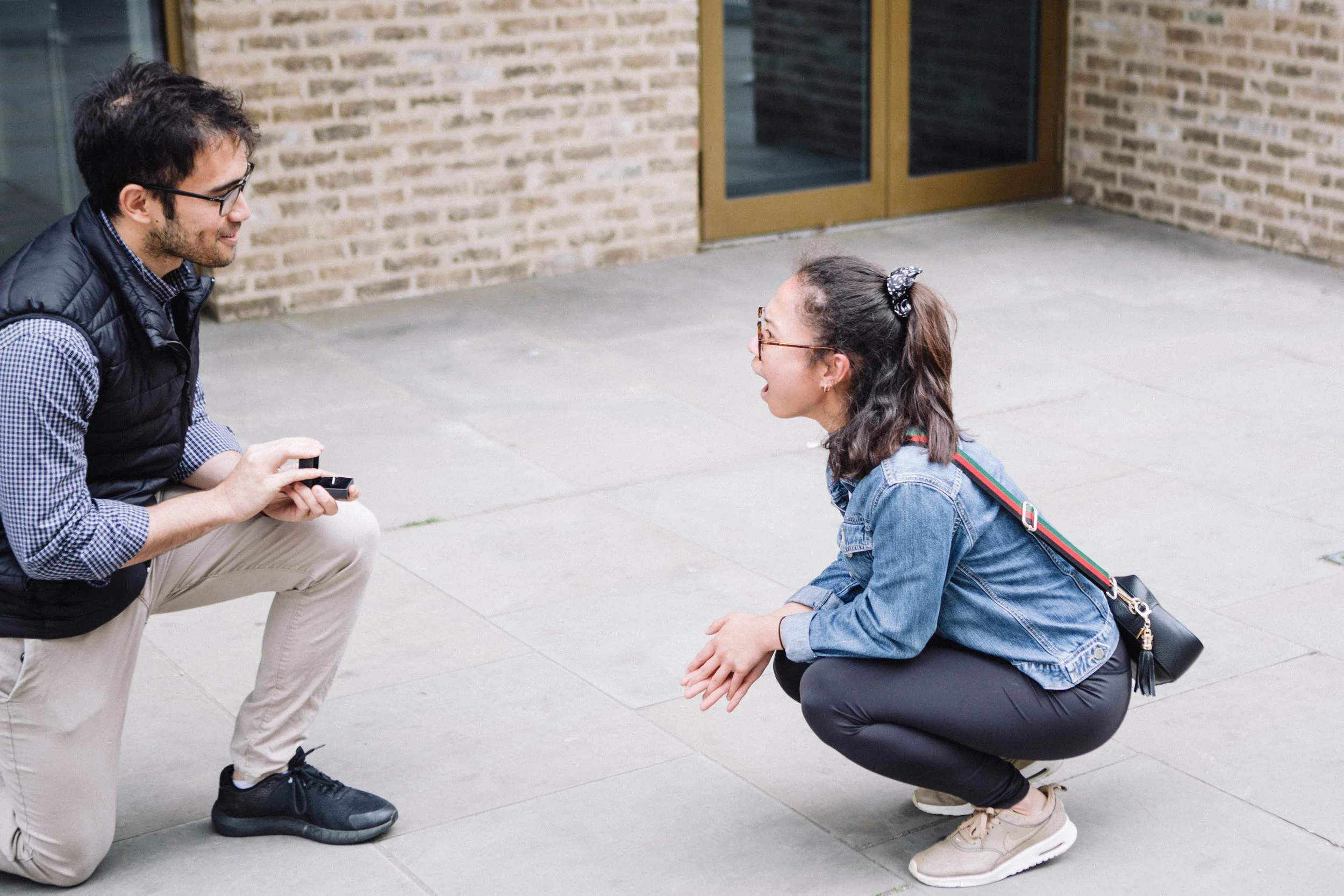 Man down on one knee to propose. Woman down on the ground with him in shock.