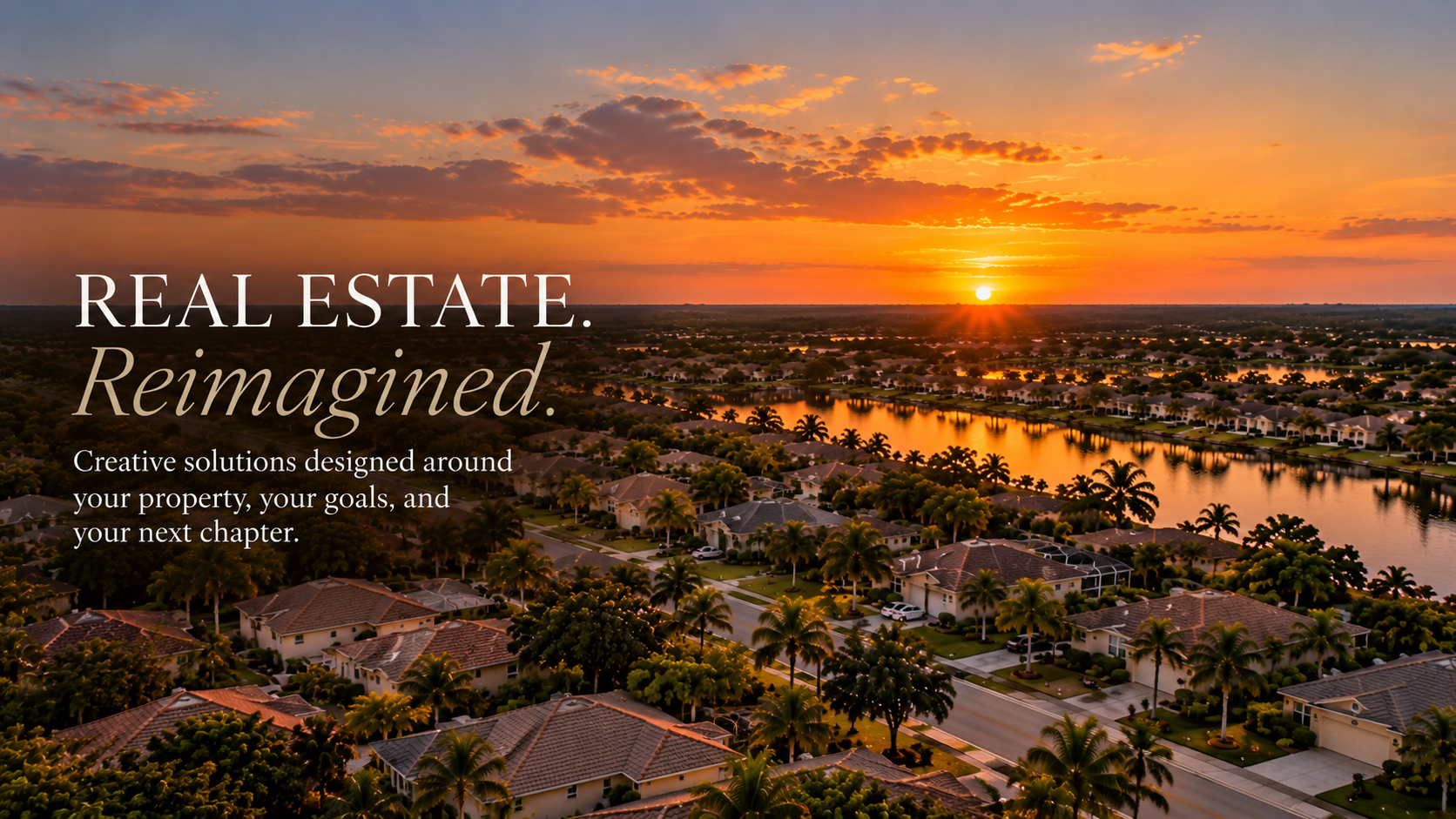 An aerial view of a suburban neighborhood at sunset, with houses, trees, and a waterway reflecting the sky's orange and purple hues.
