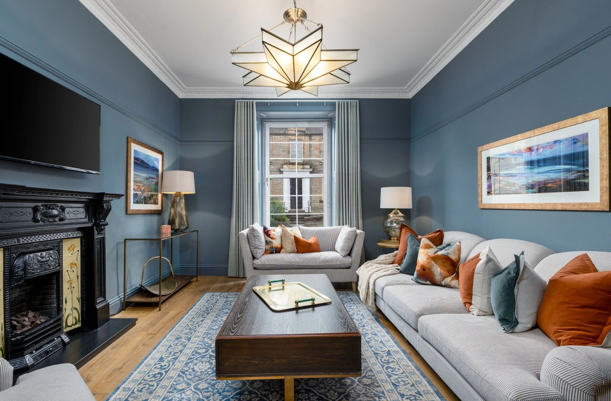 A guest living room with blue panelled walls and a chandelier, prepared for arrival